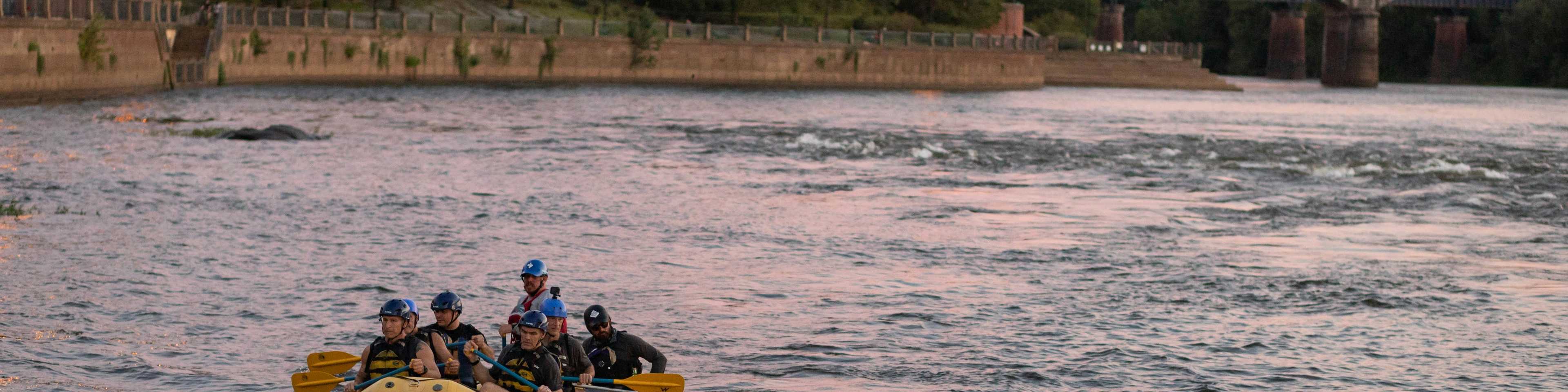 Group paddling yellow raft on scenic Central Georgia river at sunset, bridge and lush trees in background