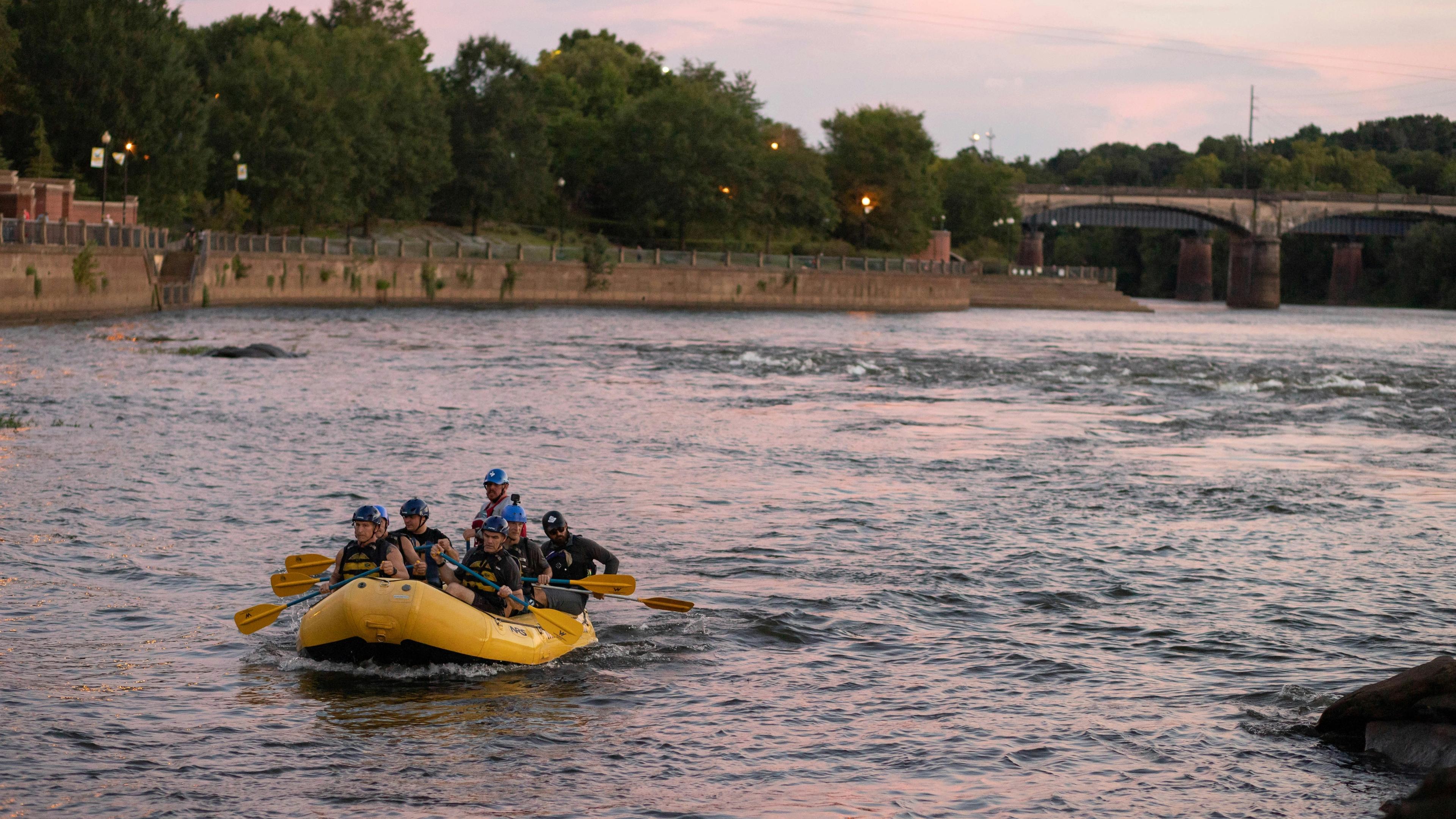 Group paddling yellow raft on scenic Central Georgia river at sunset, bridge and lush trees in background