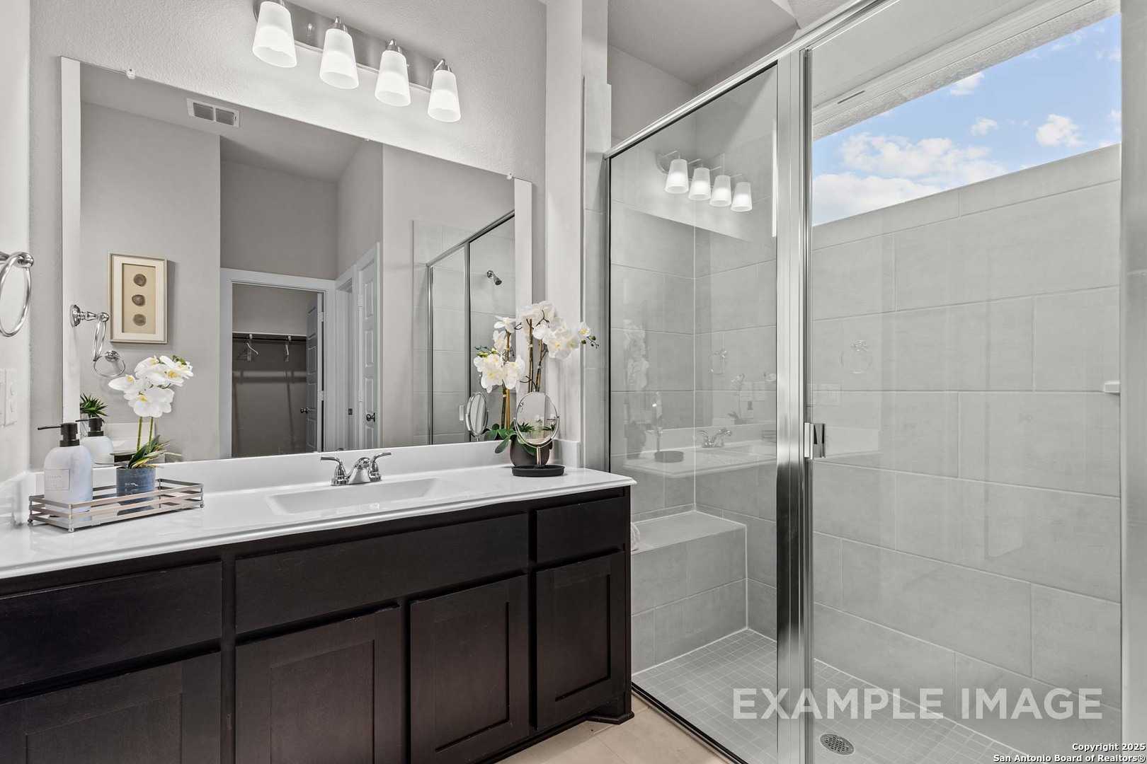 Elegant master bathroom with dark wood vanity, frameless glass shower, white orchids in The Collin B home, Seguin, Texas
