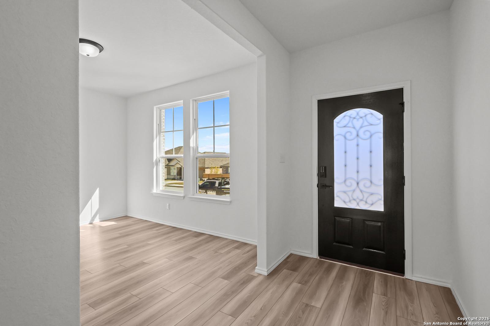 Bright entryway with hardwood floors, large windows overlooking neighborhood, arched black door in Davidson Homes The Douglas E, San Antonio
