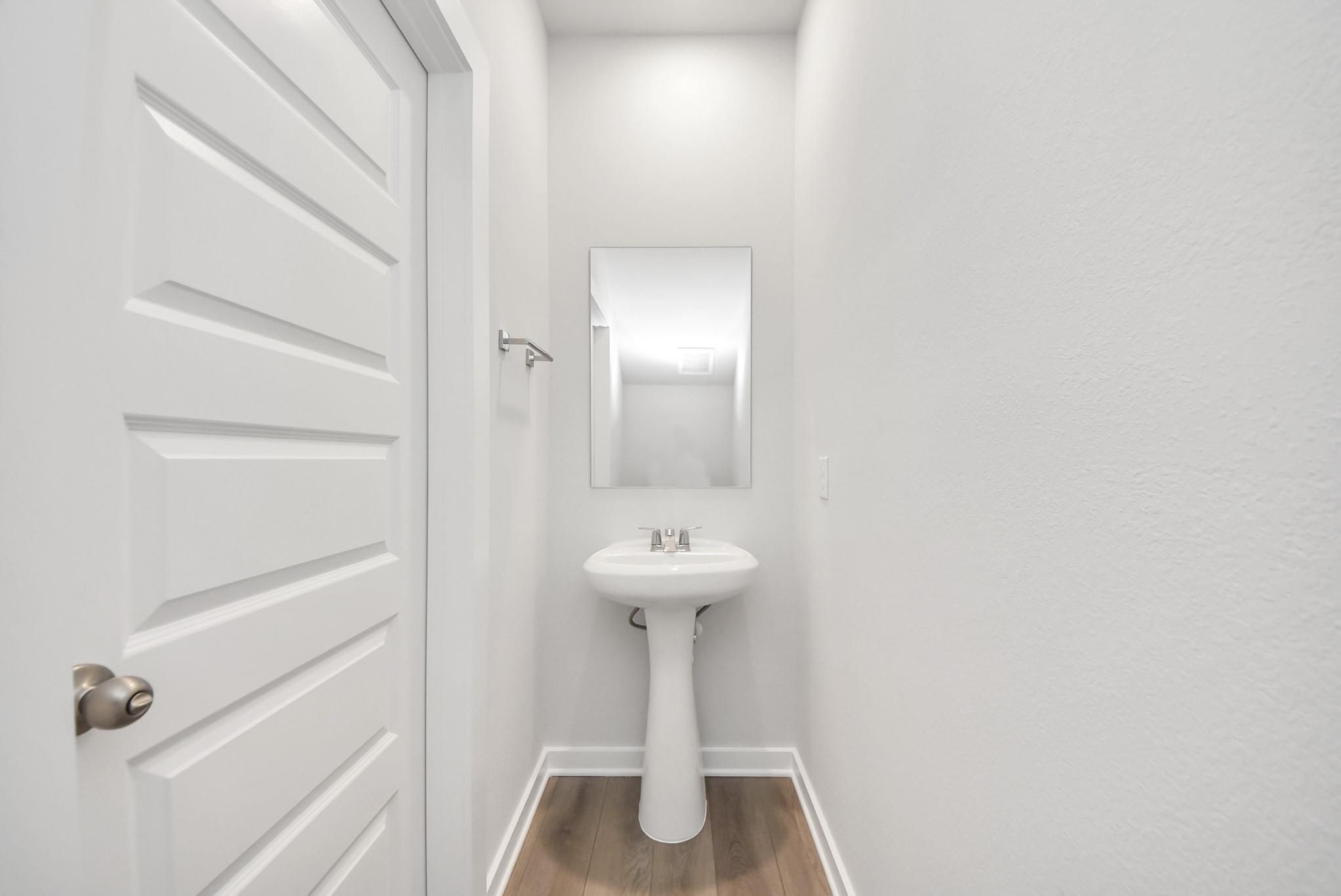 Modern half-bath with pedestal sink and mirror in The Blanco E floor plan at The Villages at WestPointe in Dayton, Texas.