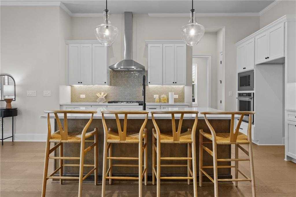 Modern kitchen with white shaker cabinets, stainless appliances, and wood island bar stools in Davidson Homes Seaside B, Woodstock, GA