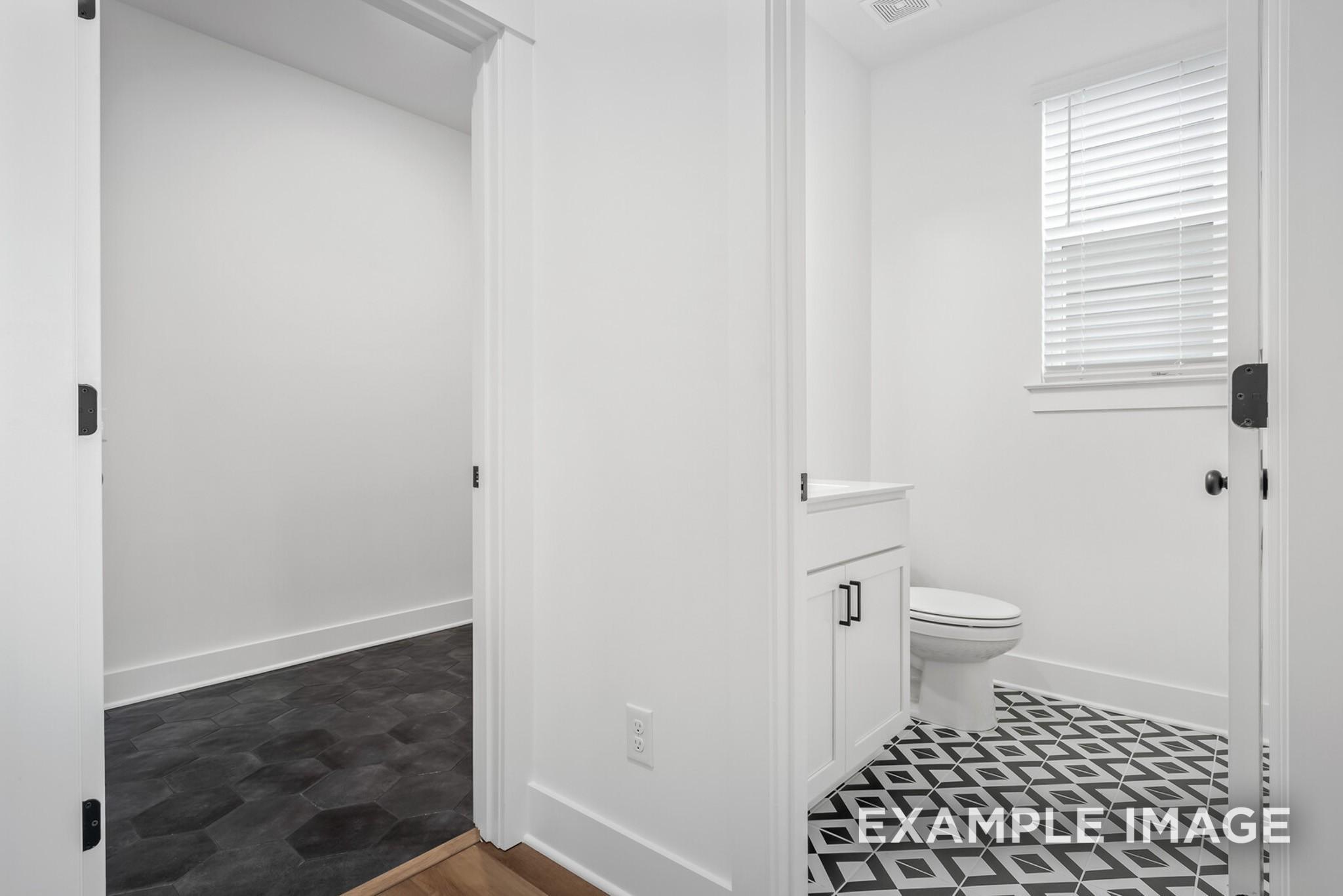 Bright white bathroom with geometric black-and-white tile floor, vanity, and toilet in Davidson Homes The Ridgeport C, Gallatin, TN