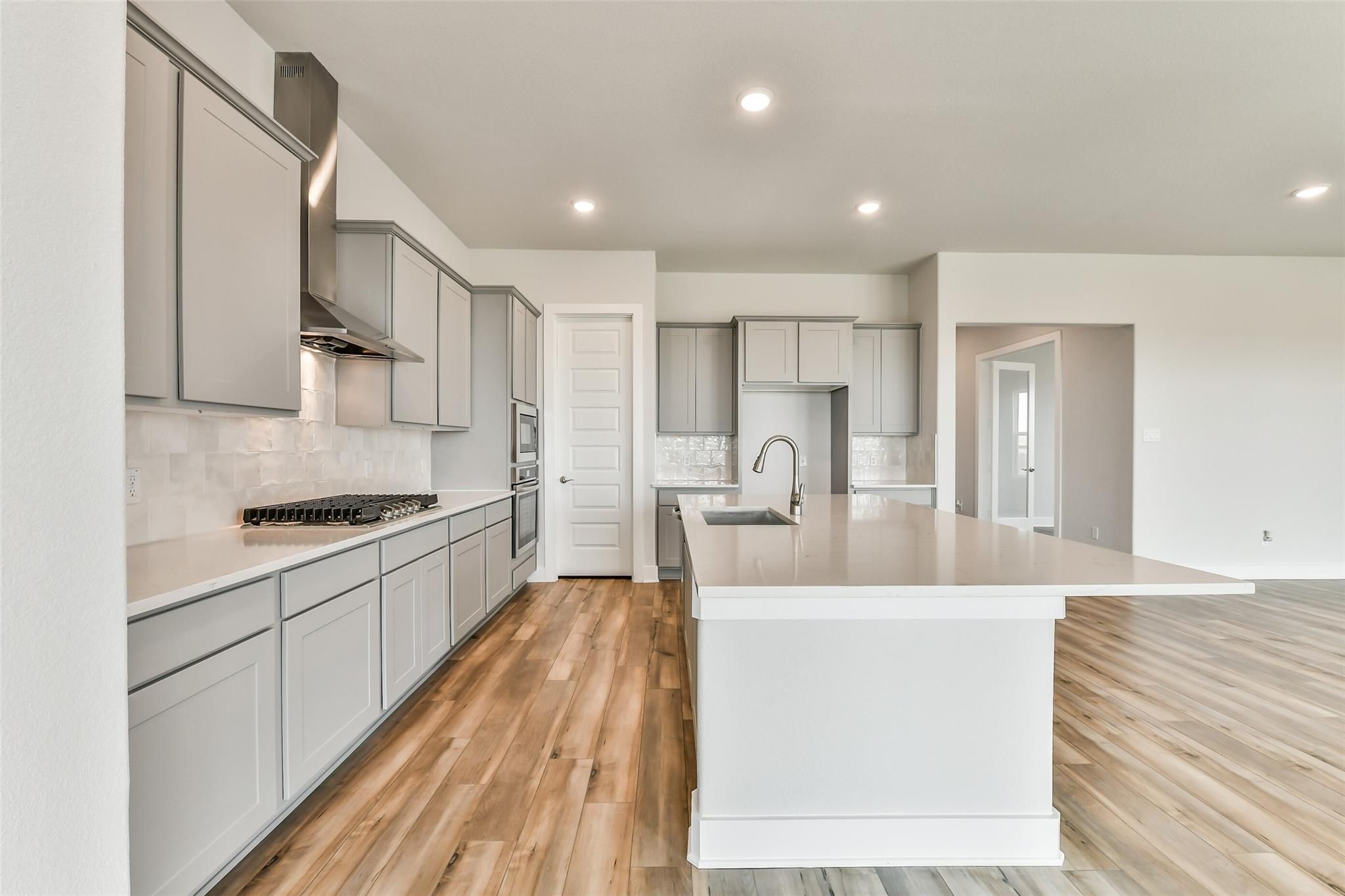 Modern gray kitchen with quartz island, stainless appliances, subway tile backsplash in Davidson Homes The George A, Lago Mar, Texas