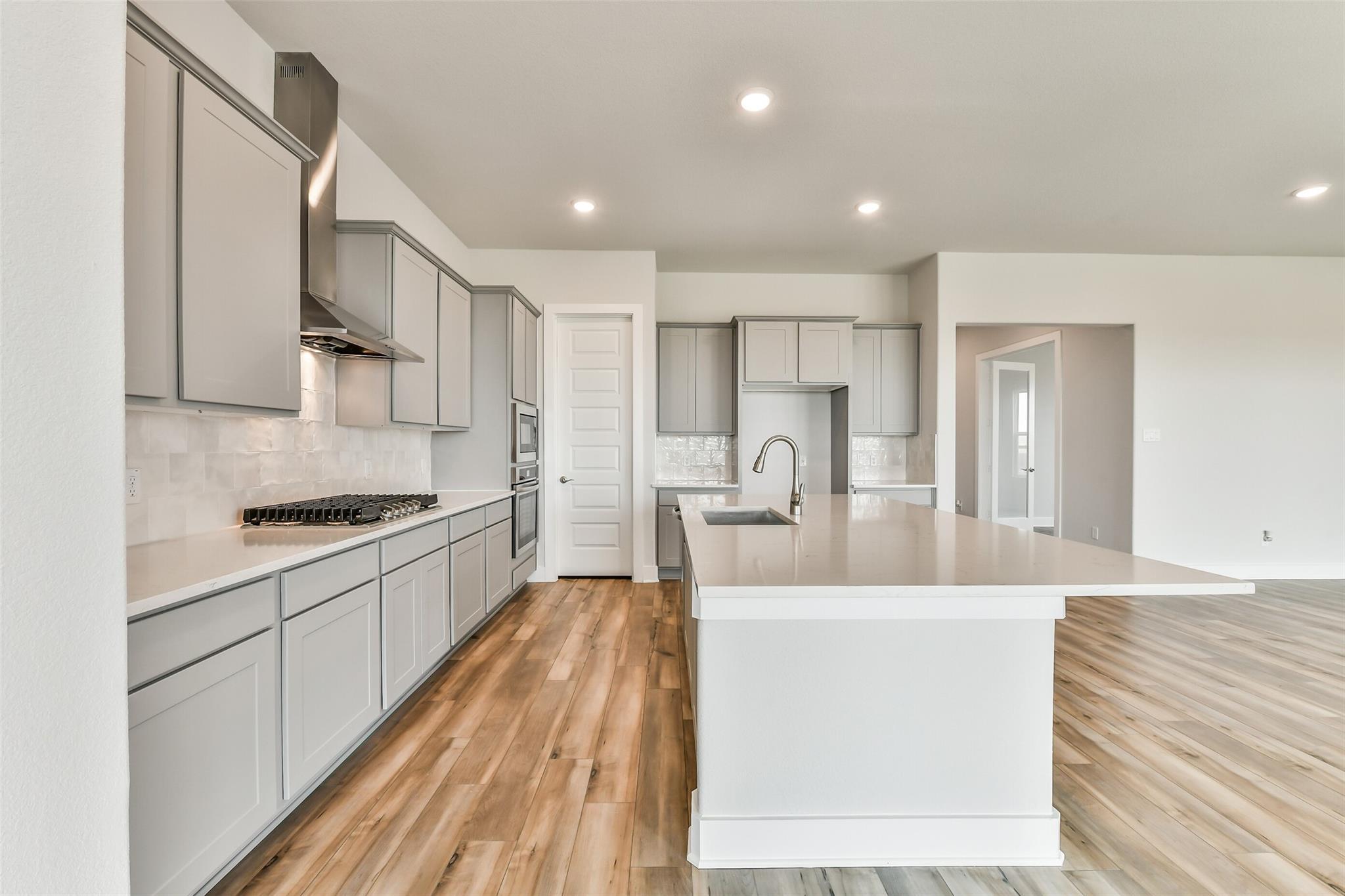 Modern gray kitchen with quartz island, stainless appliances, subway tile backsplash in Davidson Homes The George A, Lago Mar, Texas