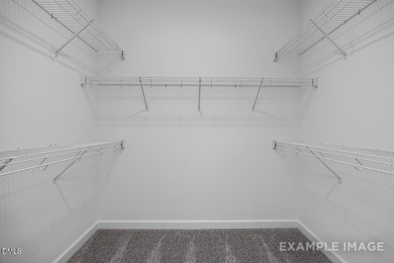 Spacious walk-in closet with white wire shelving and carpeted floor in The Magnolia D by Davidson Homes, Angier, NC