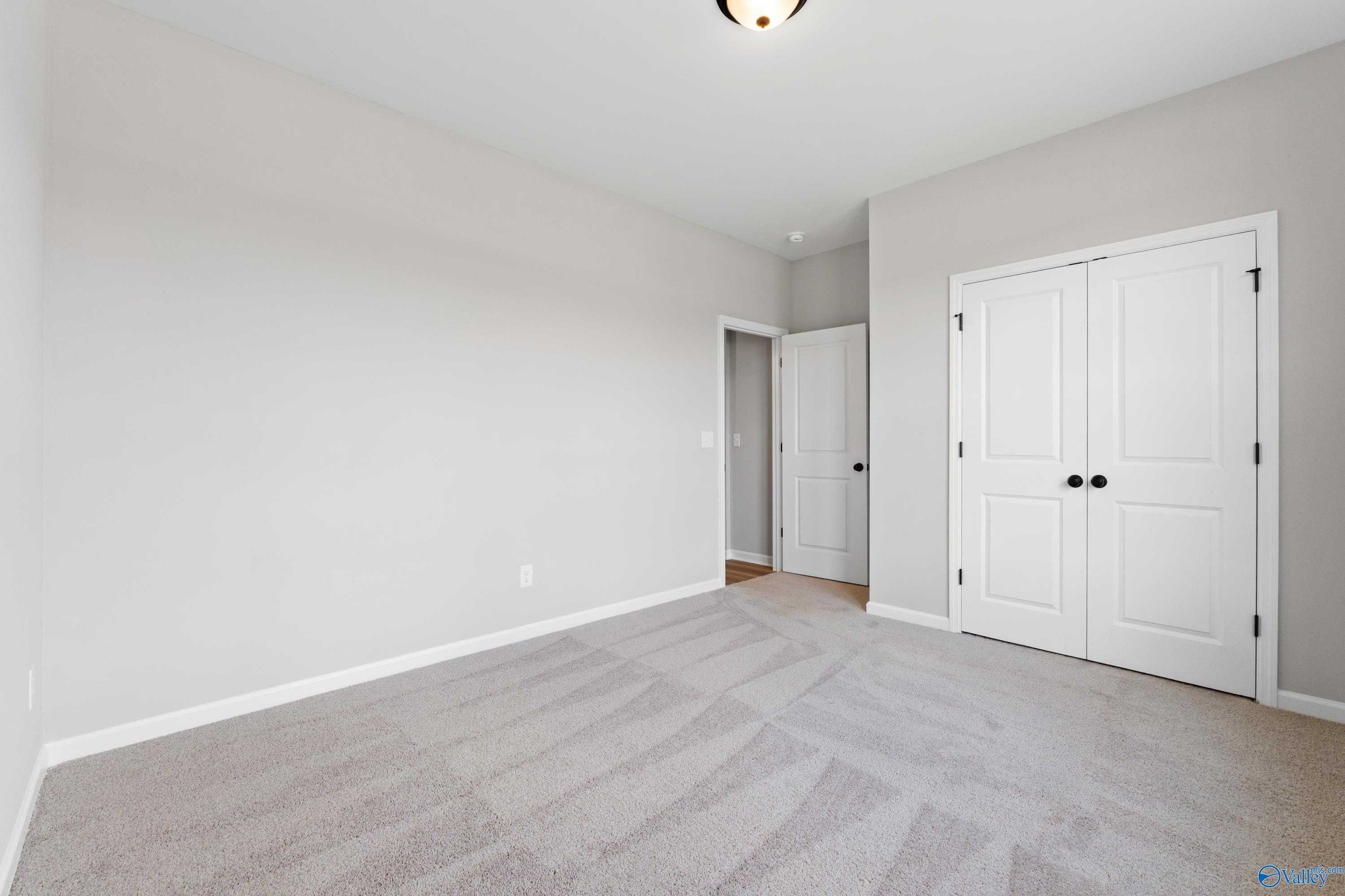 Spacious bedroom with light gray walls, neutral carpet, white double doors in Davidson Homes The Phoenix, Hazel Green, AL