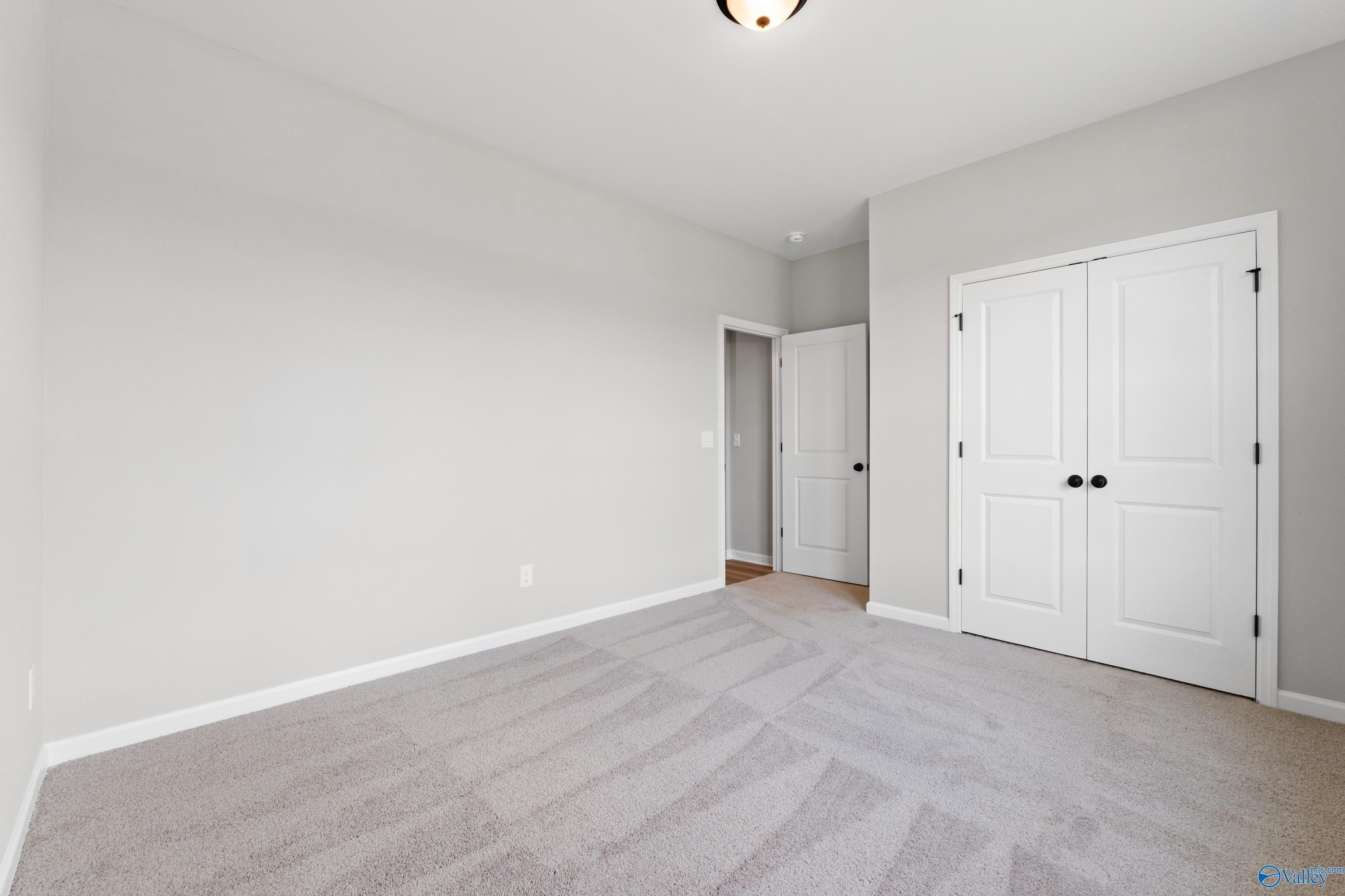 Spacious secondary bedroom featuring gray walls, carpet flooring, and double-door closet in Davidson Homes The Phoenix, Hazel Green, Alabama