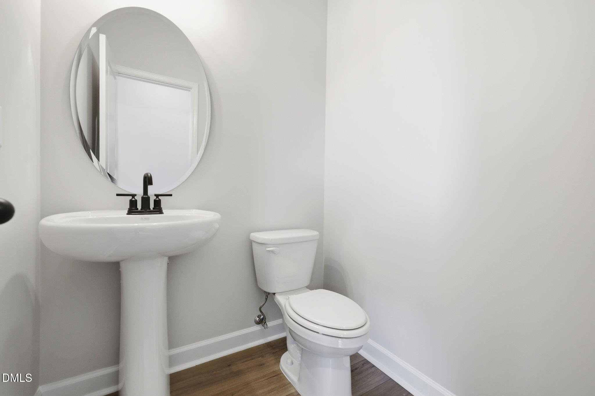 Modern powder room with pedestal sink, oval mirror, and wood flooring in The Mitchell floor plan at Camden Park, Knightdale.