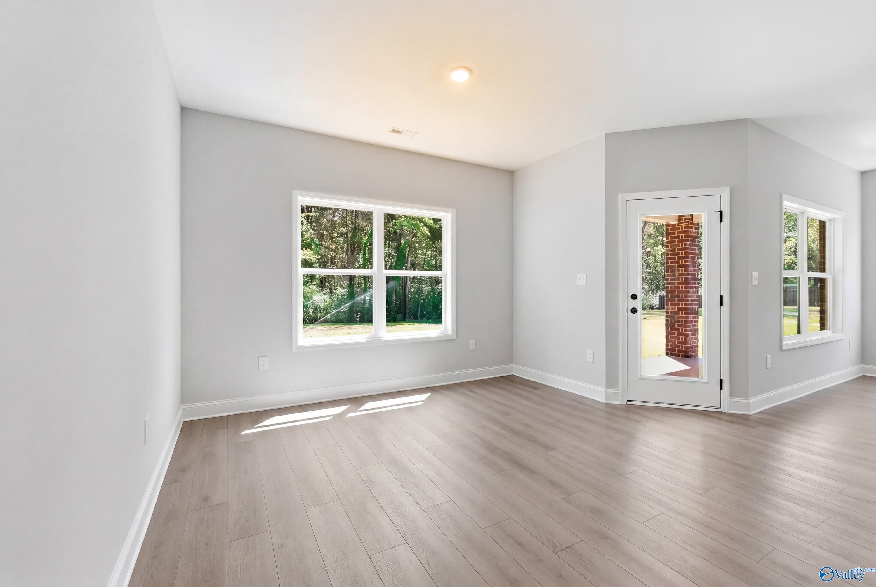 Bright room with gray walls, large windows overlooking trees, glass door to brick exterior, hardwood floors in The Franklin, Huntsville AL