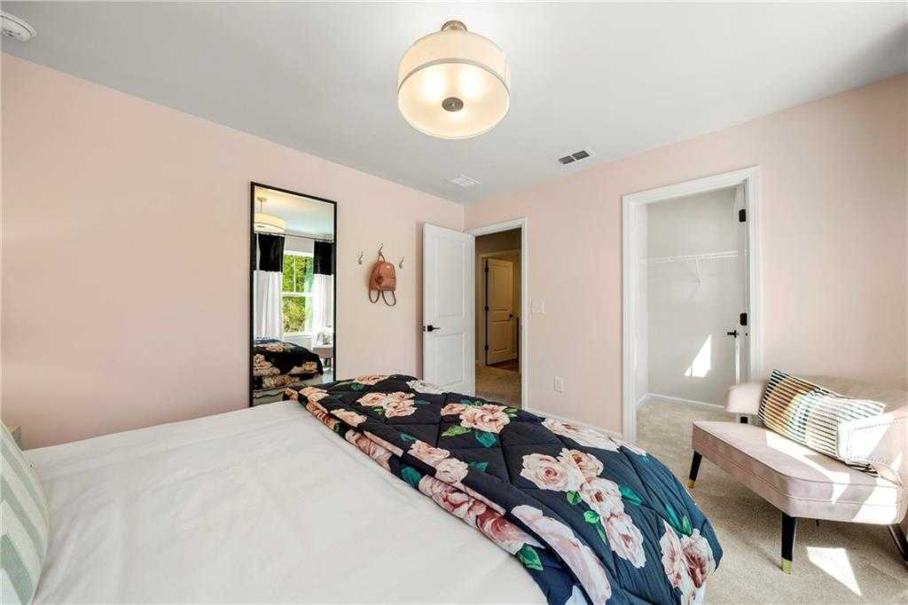 Cozy bedroom with pink walls, floral comforter on bed, full-length mirror, and bench in Davidson Homes The Hickory B, Riverwood, Dallas, GA