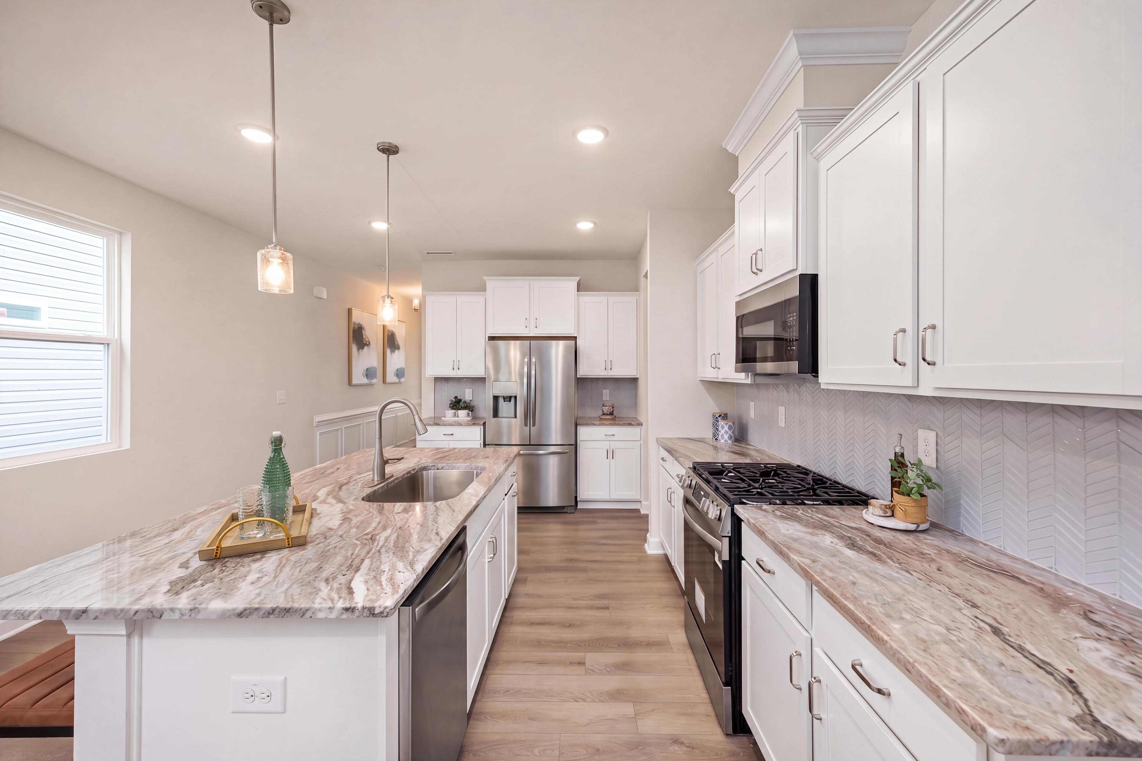 Modern kitchen at Gregory Village in Lillington, NC by Davidson Homes featuring white cabinets and stone countertops.