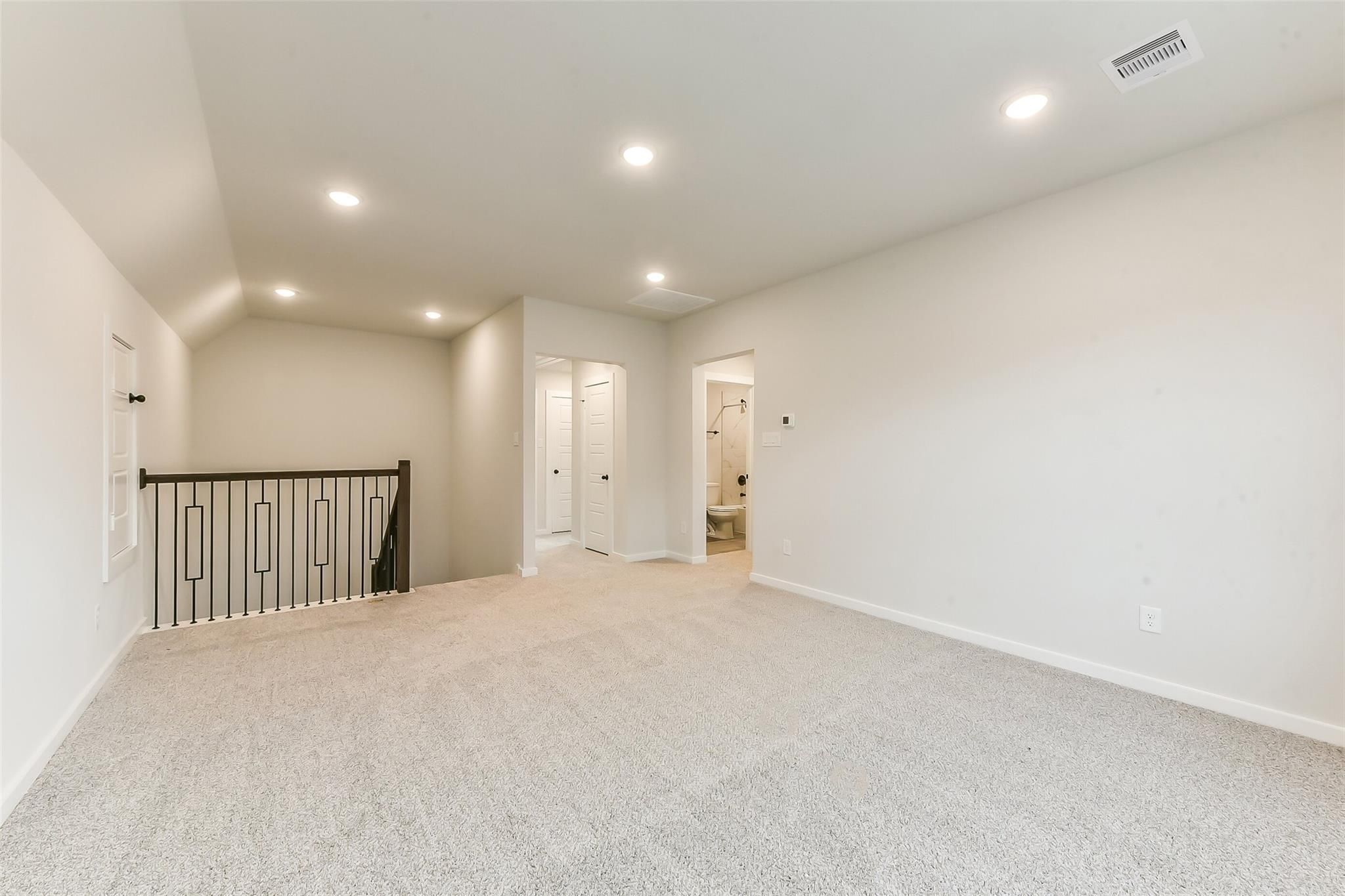 Spacious upstairs loft with beige carpet, black metal railing, bedroom doors, and adjacent bathroom in Davidson Homes The Sequoia C, Crosby Texas