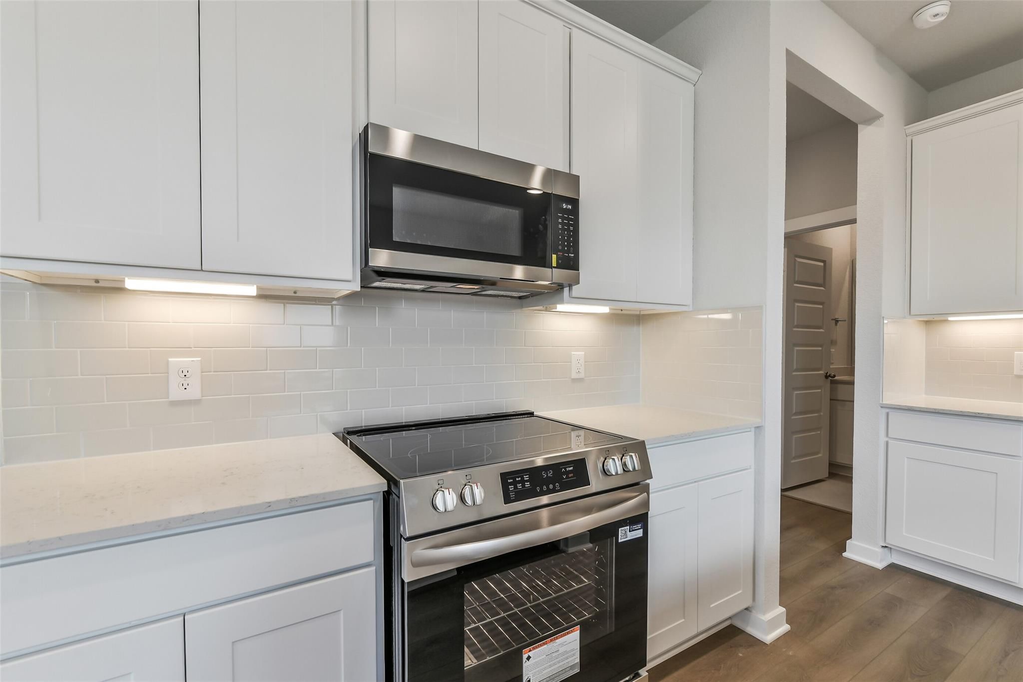 Modern kitchen with white shaker cabinets, stainless steel microwave, oven, and quartz countertops in Davidson Homes The Frio G, Cleveland, Texas