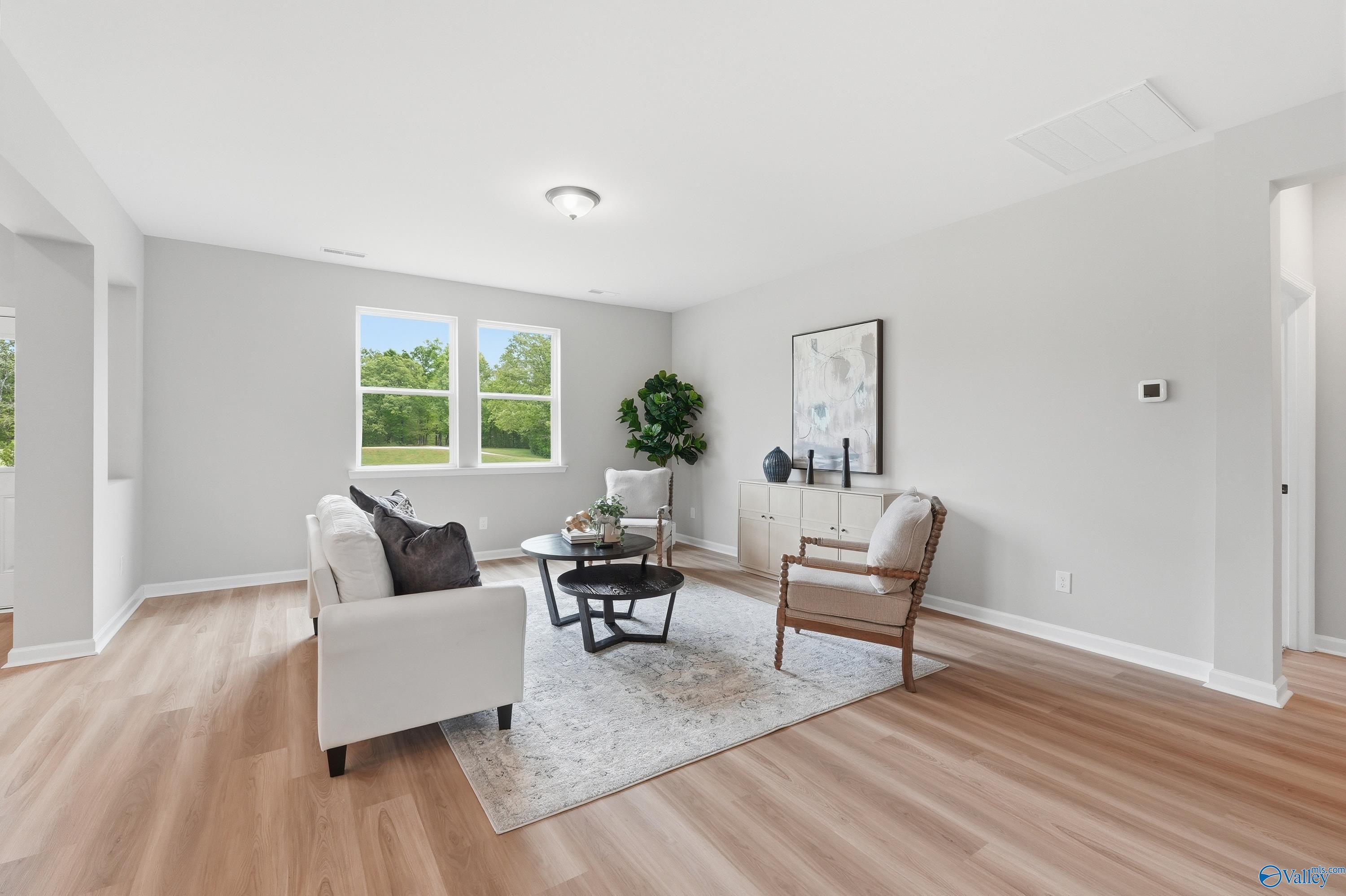 Cozy living room with white sofa, rattan chair, fiddle leaf plant, and lush backyard view in Davidson Homes The Dorado, Huntsville, Alabama