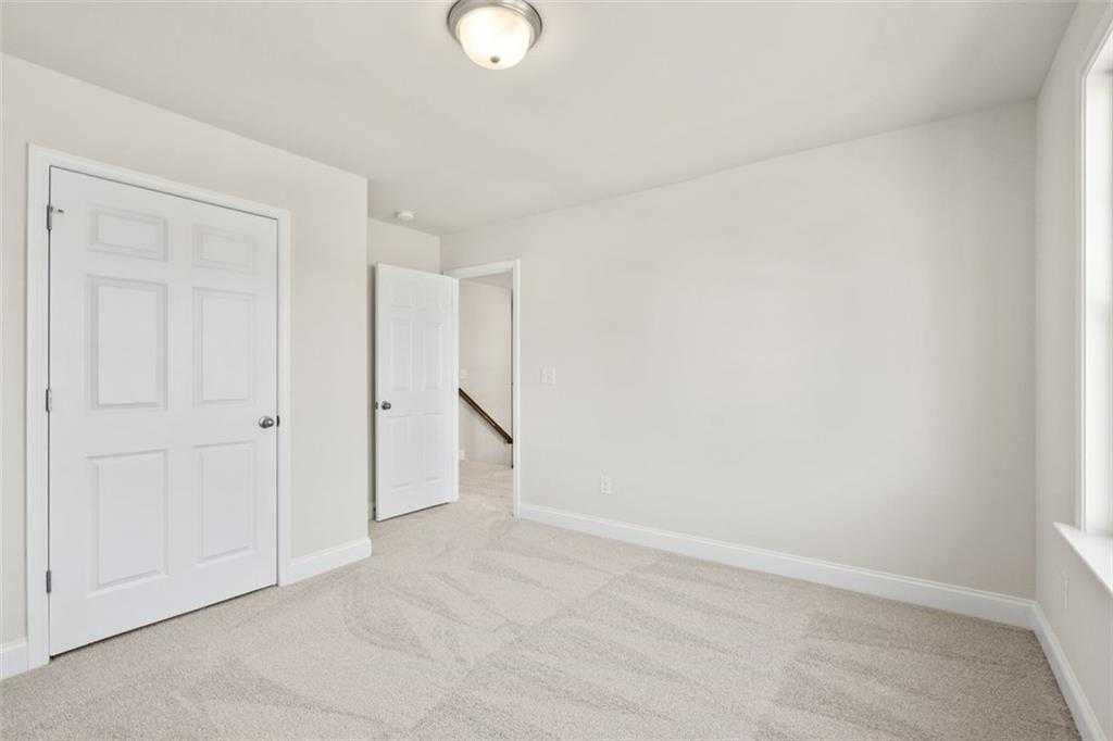 Bright empty bedroom with white walls, beige carpet, closet door, and hallway access in Davidson Homes The Ash C, Hoschton, GA