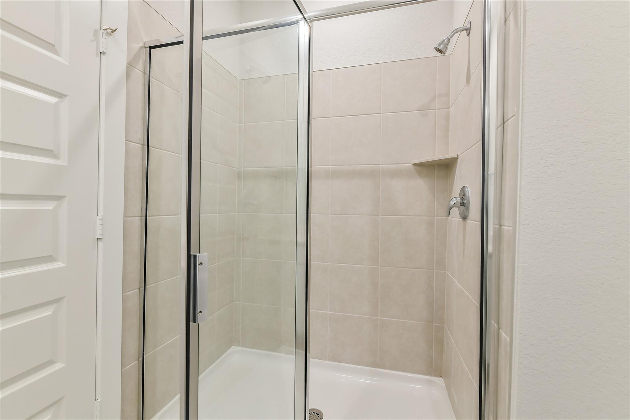 Modern glass shower with frameless doors and beige subway tiles in Davidson Homes The Frio G, Conroe Texas
