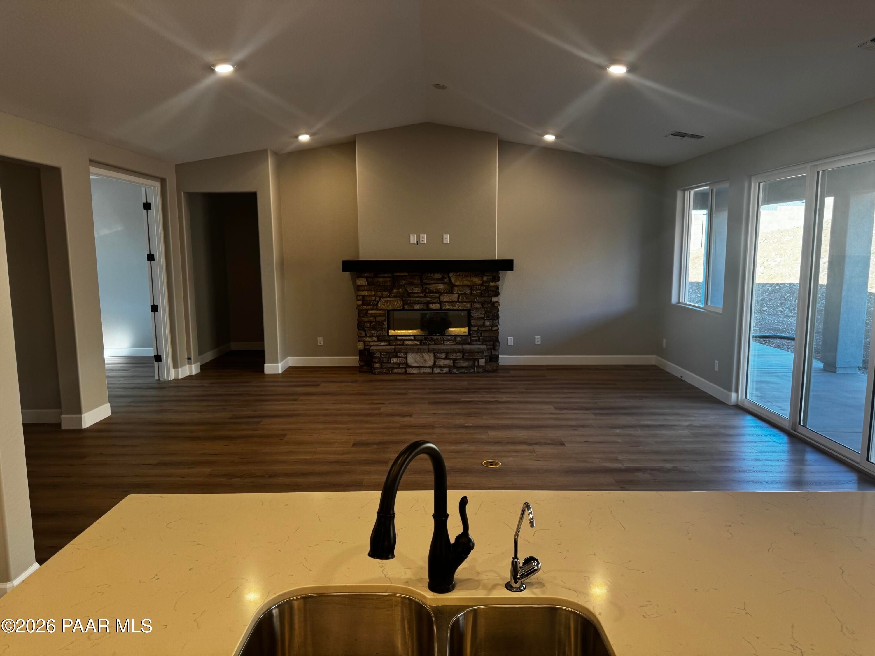 Open-concept great room with stone fireplace, kitchen island sink, and large sliding doors in The Monarch B by Evermore Homes, Prescott Valley, AZ