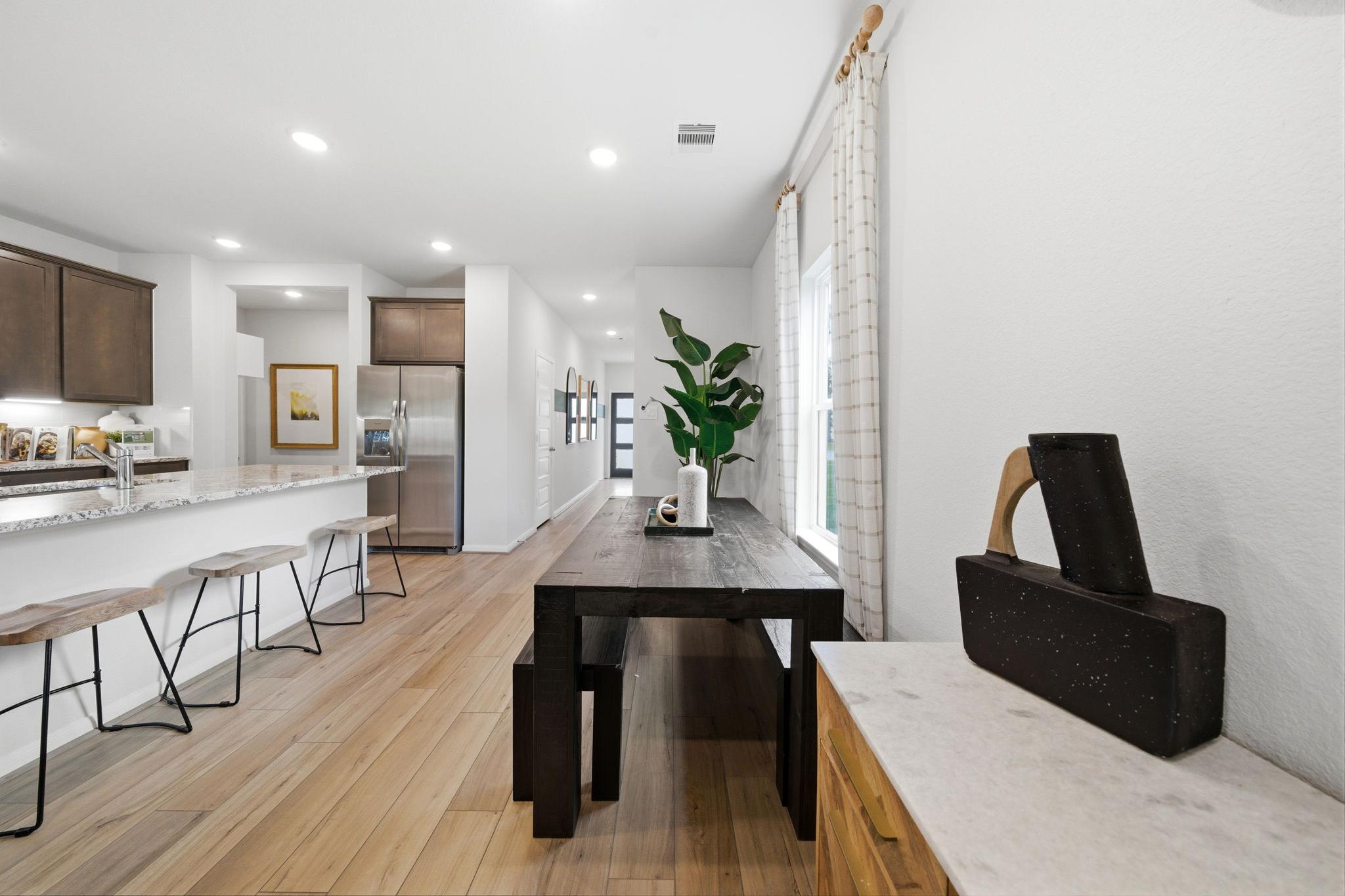 Open-concept kitchen and dining area at Caney Creek Place in Conroe TX with hardwood floors, white cabinets, and wooden table