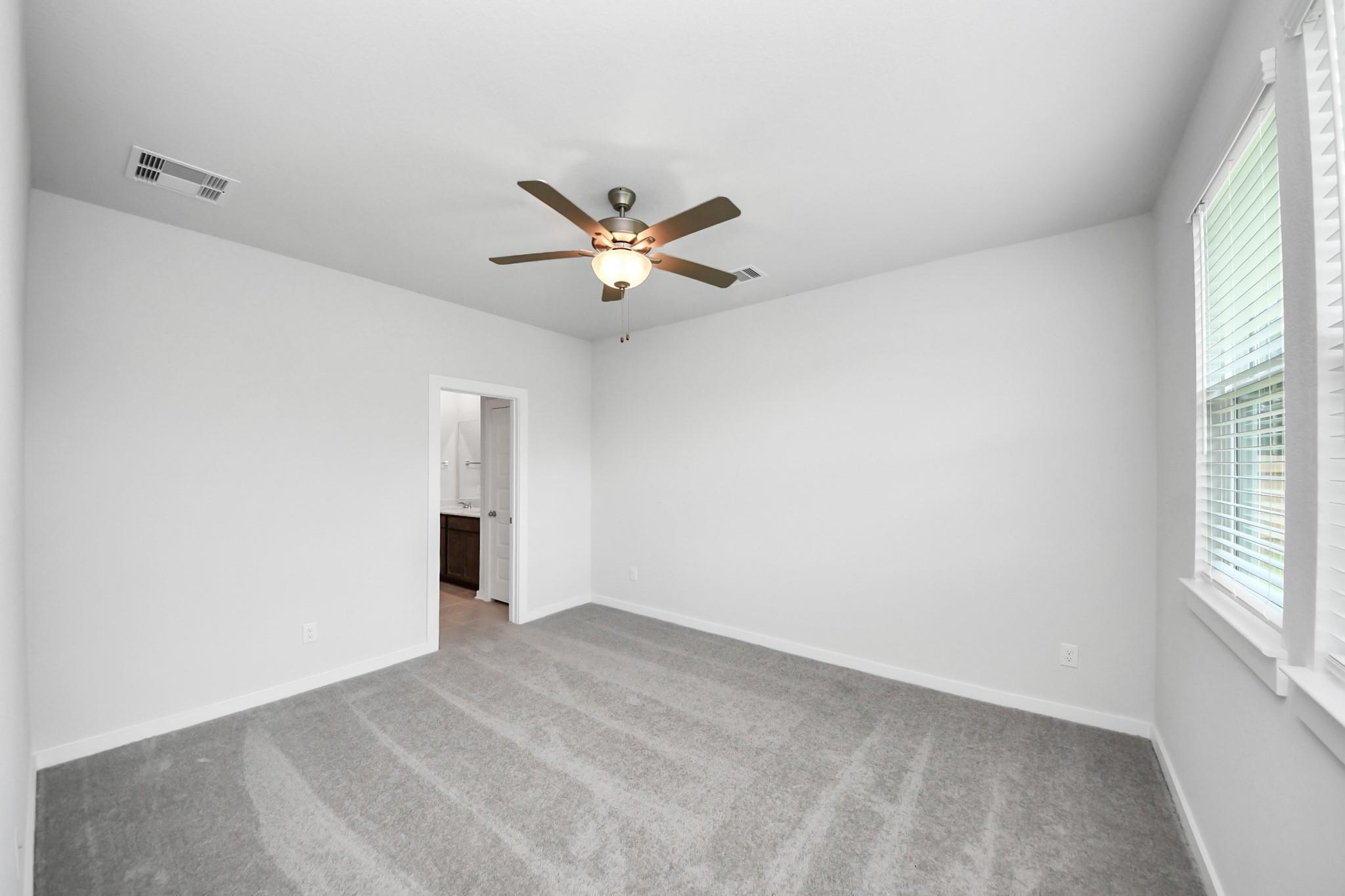 Spacious bedroom with ceiling fan and carpeted floors in The Brazos F floor plan at Liberty Estates, Cleveland, Texas.
