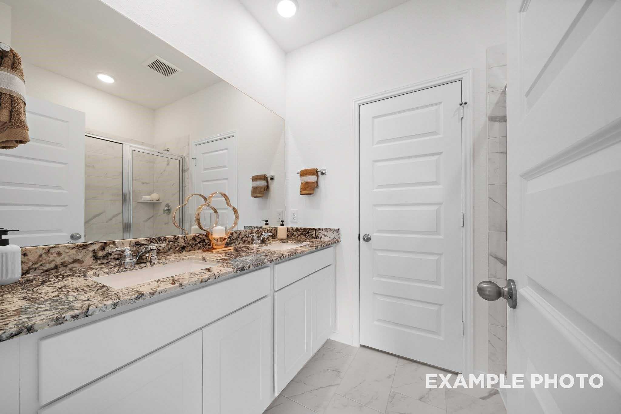 Elegant master bathroom with double granite vanity, frameless glass shower, and white shaker cabinets in Davidson Homes The Sabine F, Magnolia, Texas