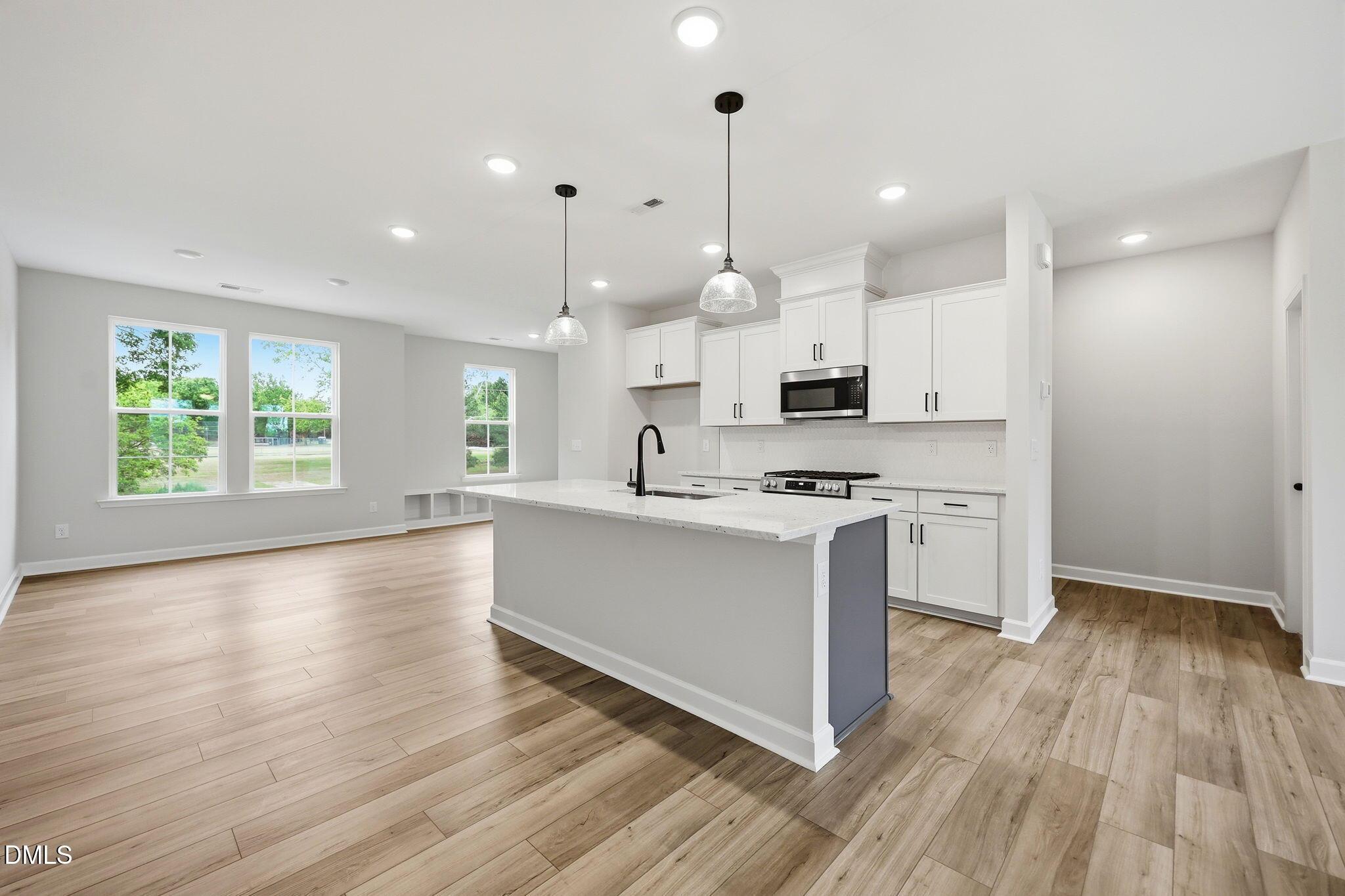 Modern kitchen with white cabinets, island, and wood floors in The Mitchell Interior floor plan, Camden Park, Knightdale.