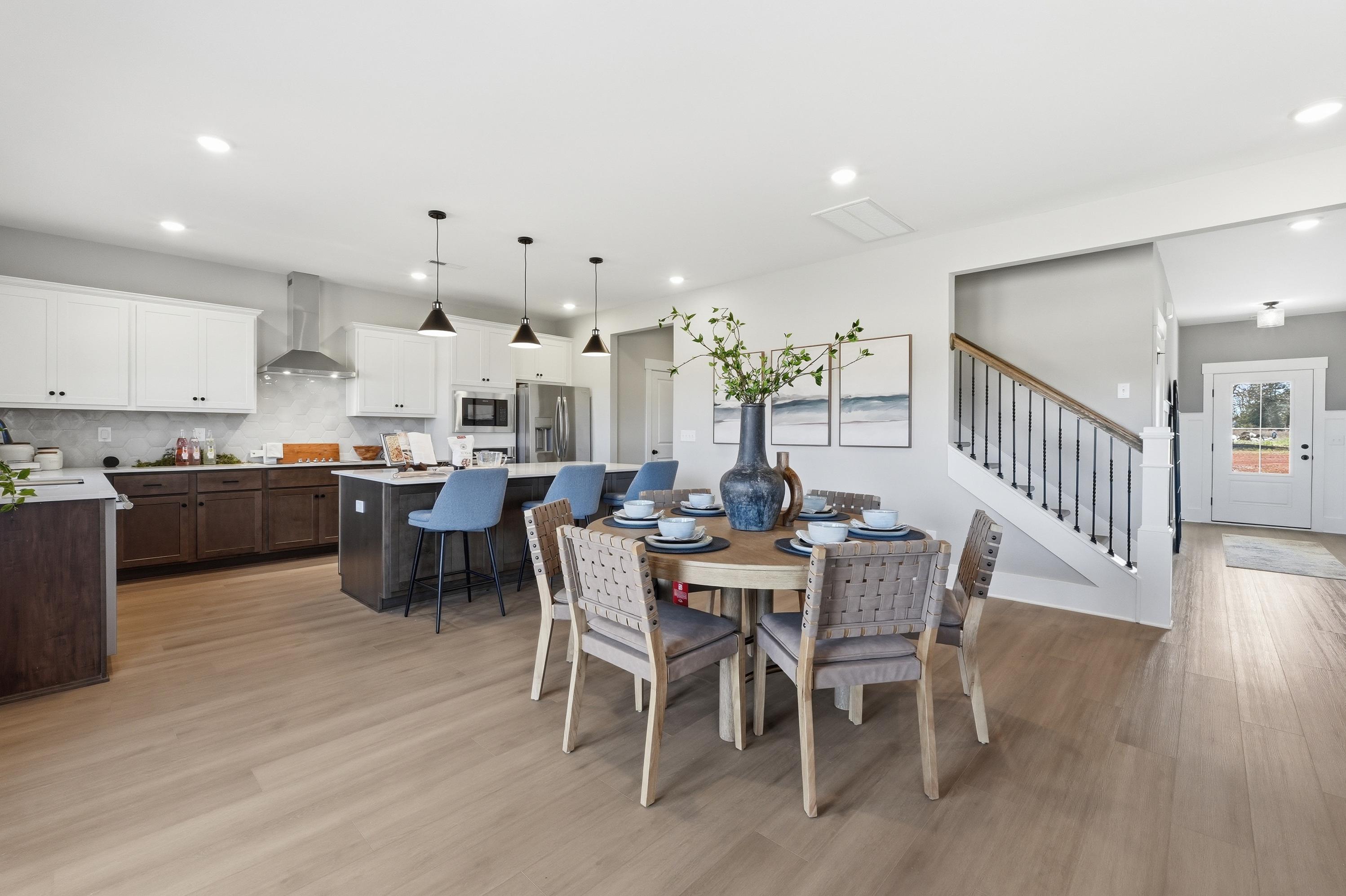 Modern open-concept kitchen and dining in Berry Cove New Market AL with island bar stools round table staircase and hardwood floors