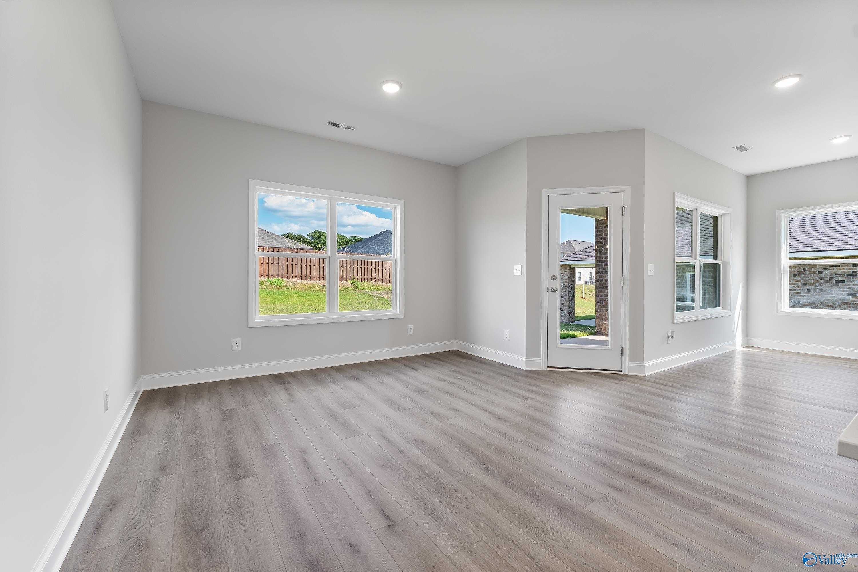 Bright family room with large windows, gray walls, luxury vinyl flooring, and glass door to green backyard in Davidson Homes The Franklin C, Toney, Alabama