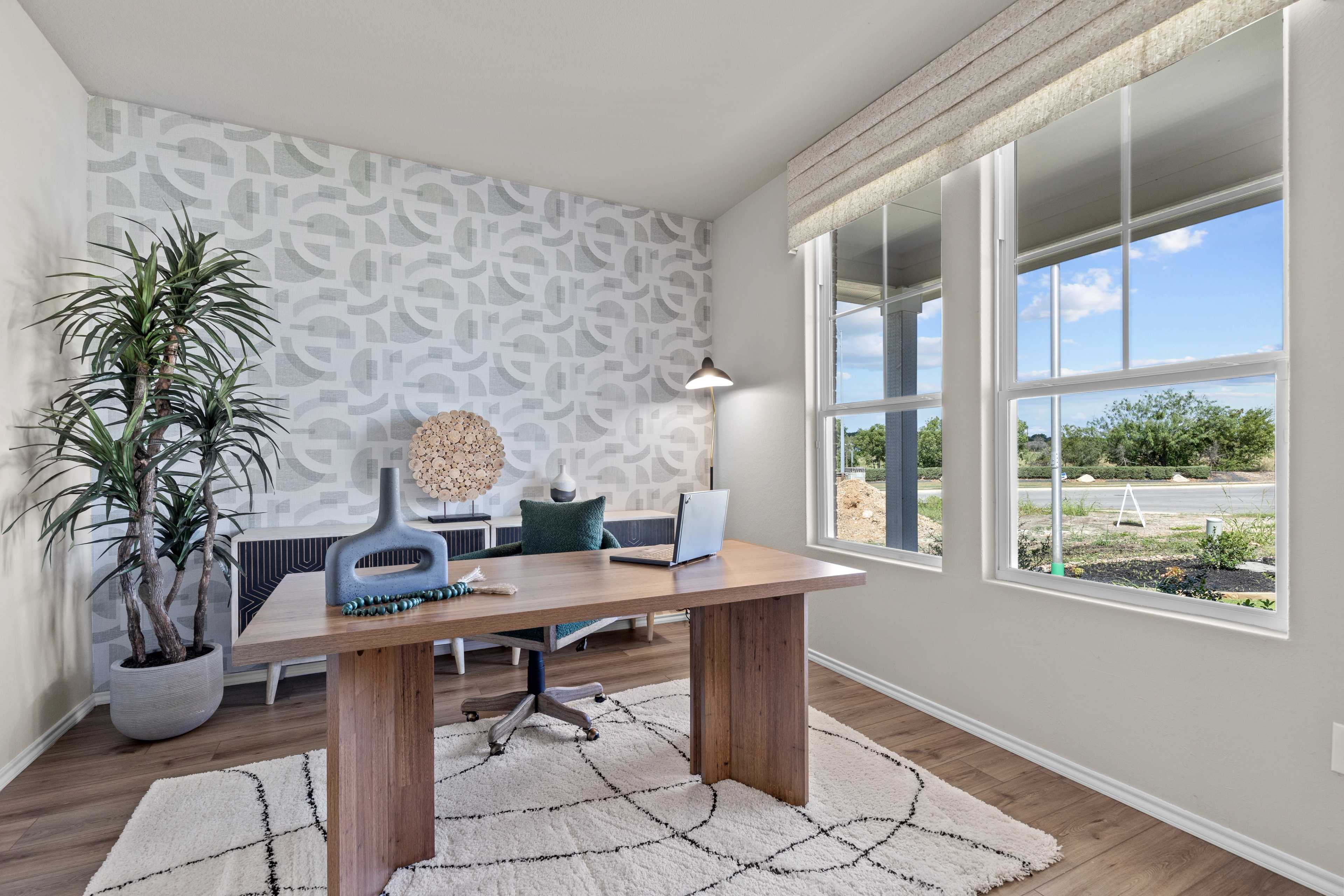 Modern home office in Comanche Ridge San Antonio with wooden desk, large windows, potted palm, and patterned accent wall