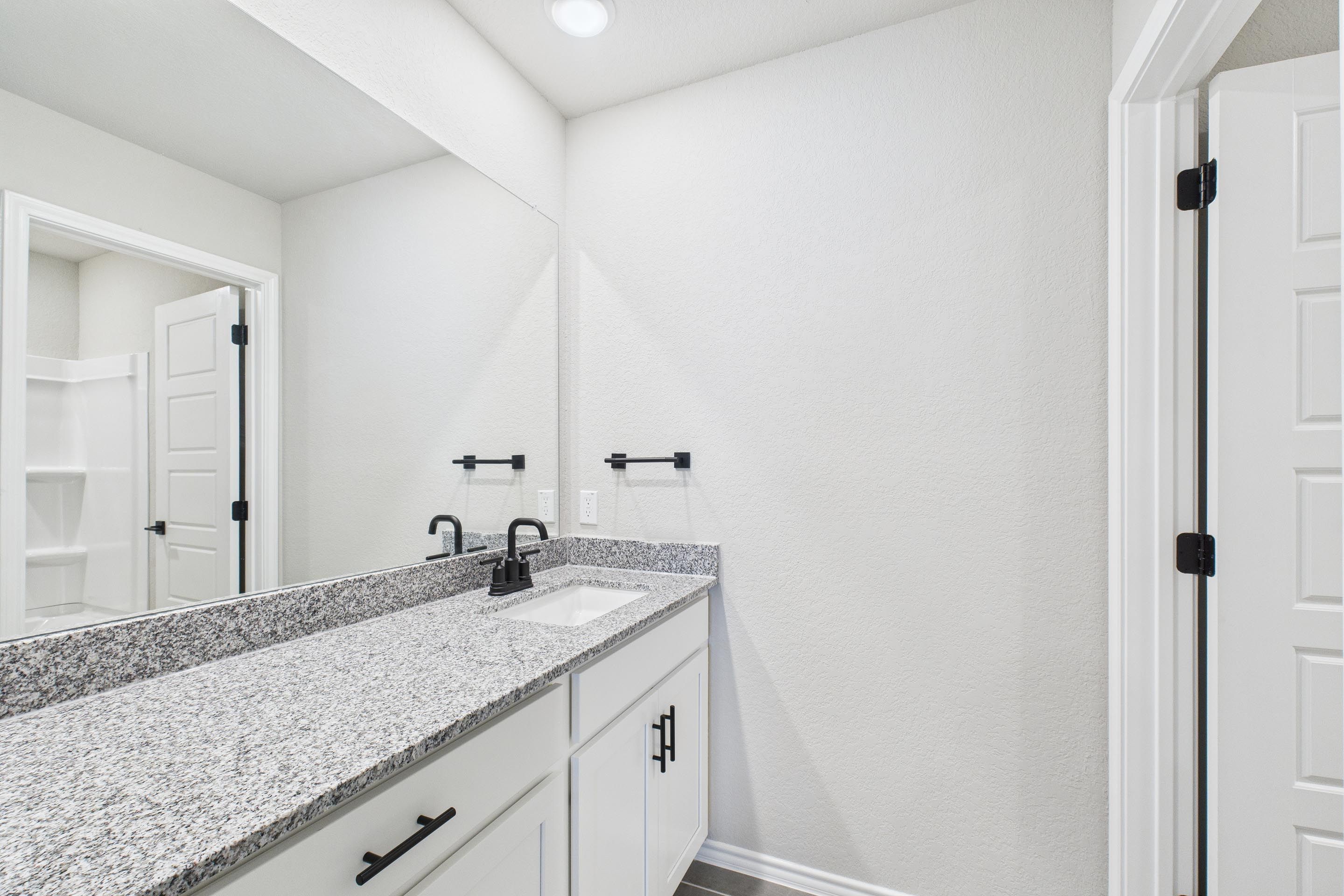 Modern bathroom in The Charlotte A featuring a granite vanity, white cabinetry, and matte black fixtures.