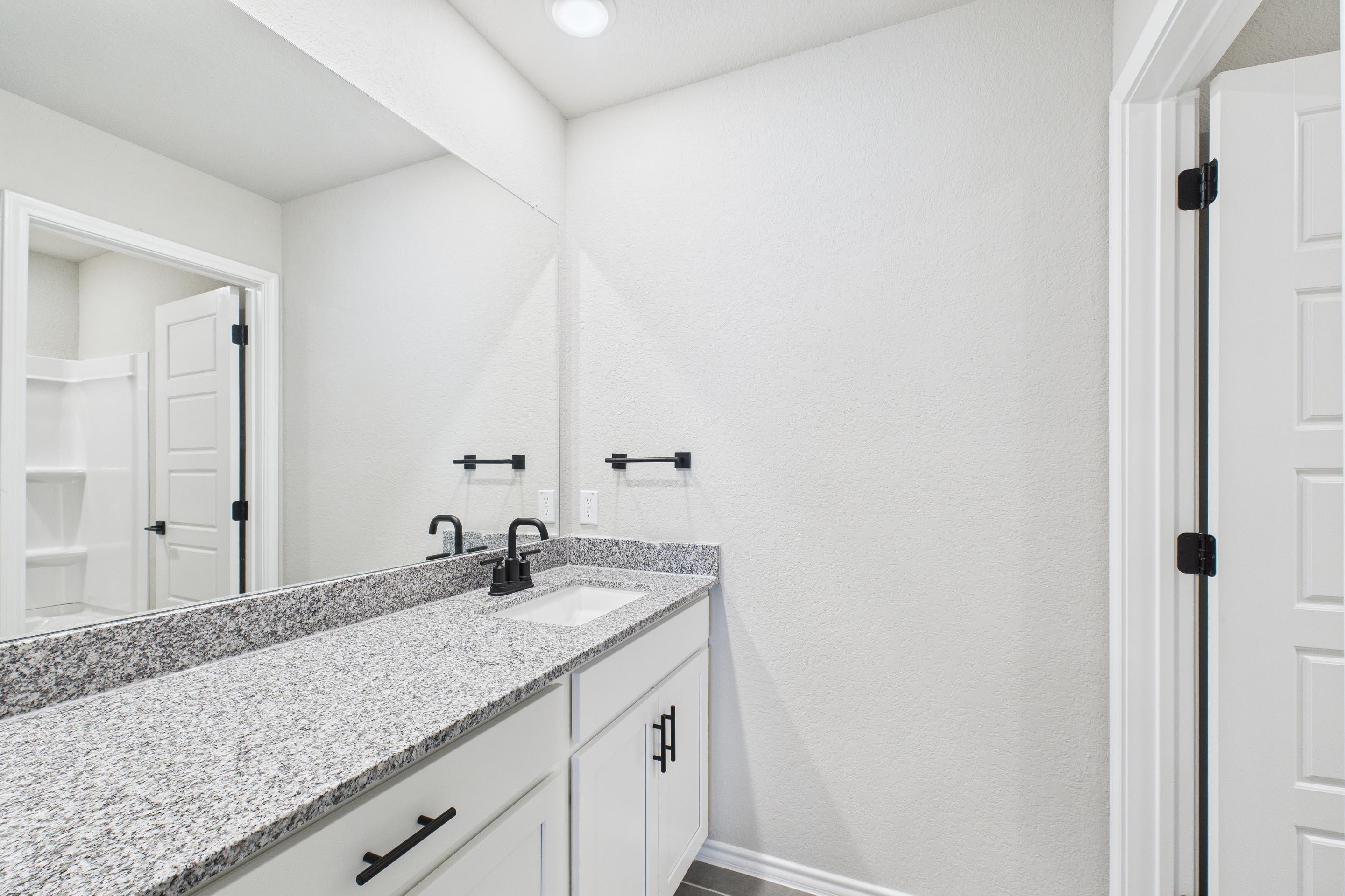 Modern bathroom in The Charlotte A featuring a granite vanity, white cabinetry, and matte black fixtures.