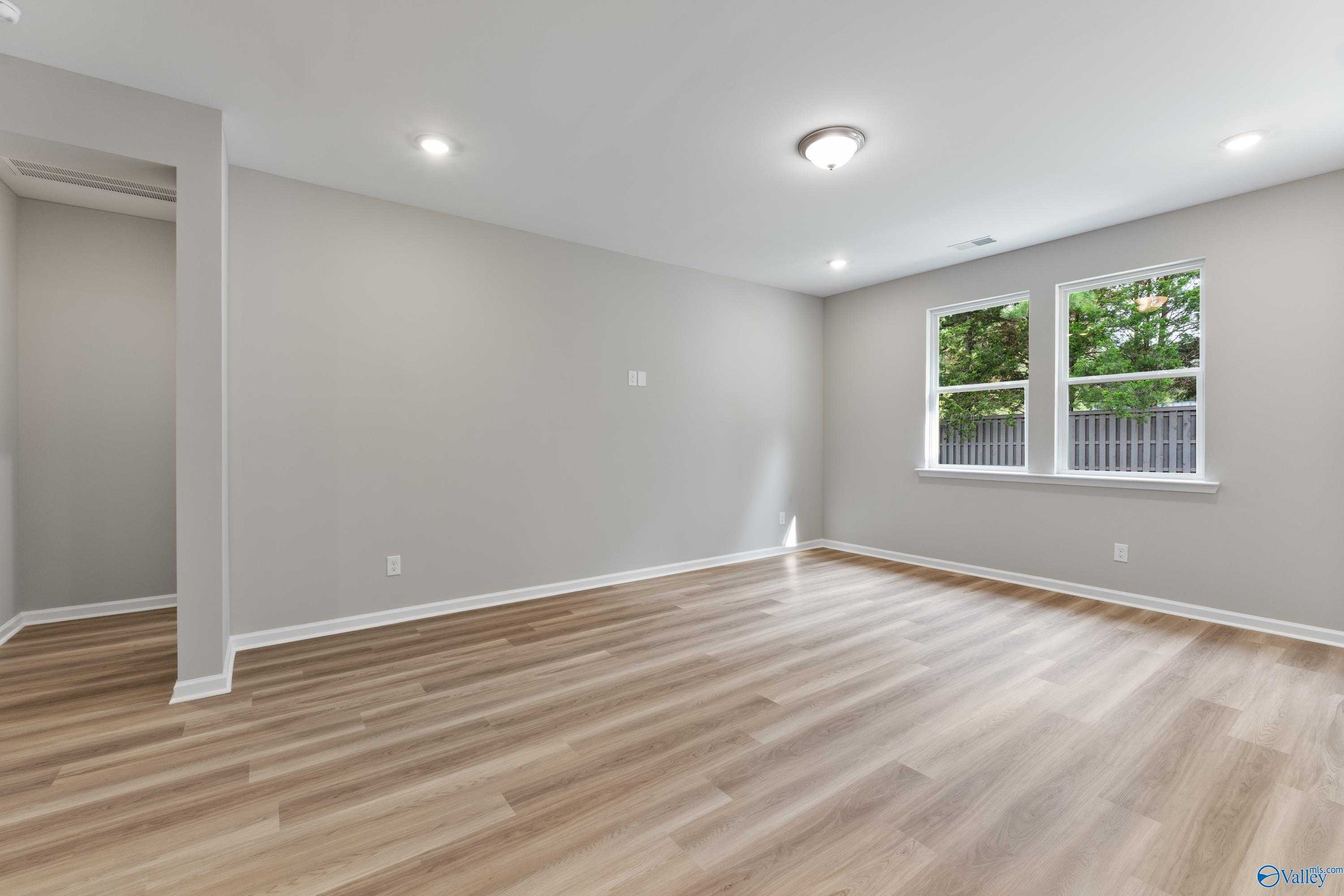 Bright bedroom with gray walls, luxury vinyl plank floors, large windows to green backyard in Evermore Homes The Grace, Madison Alabama