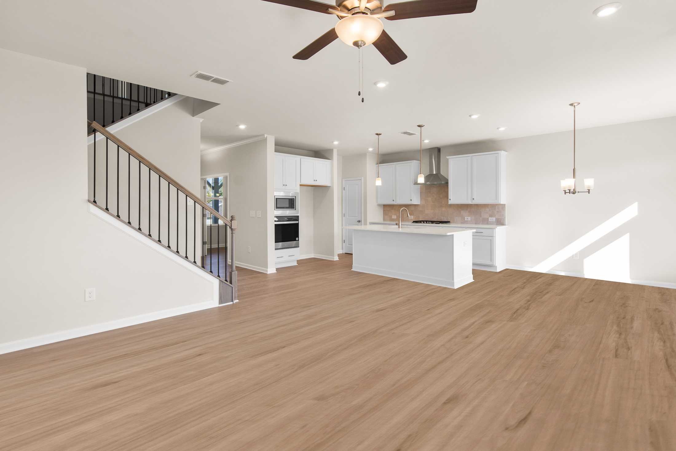 Spacious open-concept kitchen in The Willow B featuring white island, stainless appliances, hardwood floors, and wrought iron stairs
