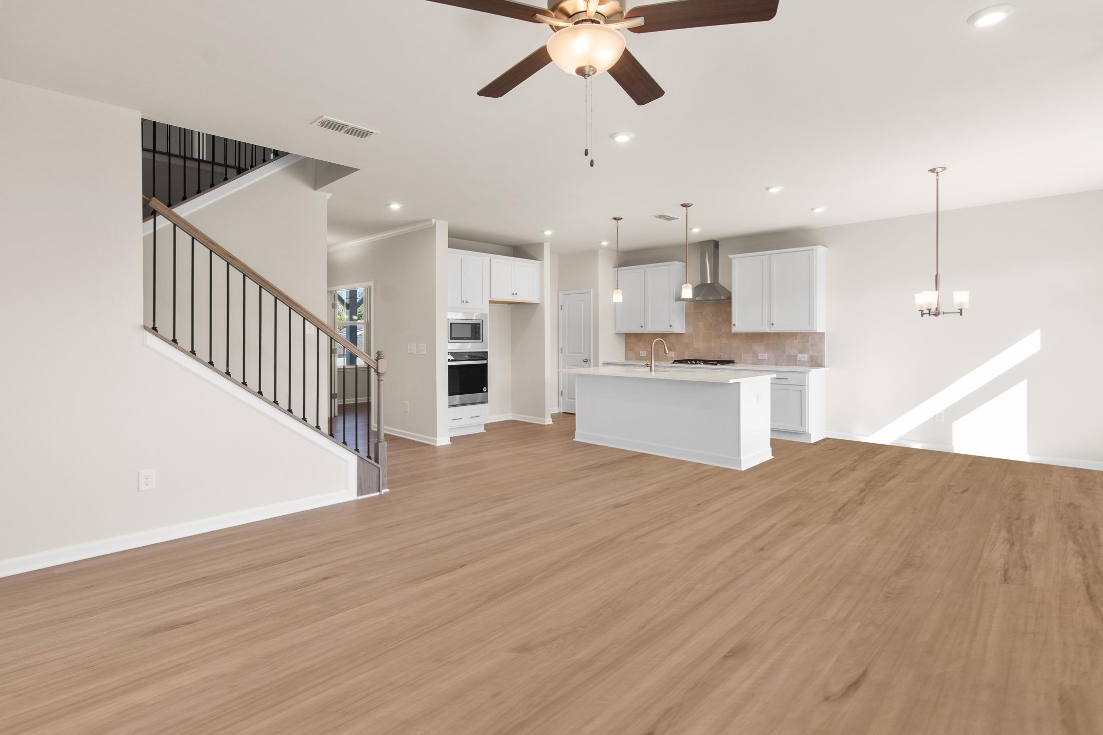 Spacious open-concept kitchen in The Willow B featuring white island, stainless appliances, hardwood floors, and wrought iron stairs