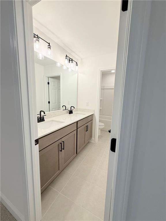 Double vanity bathroom with modern light fixtures and tile flooring in The Hickory B at Wehunt Meadows, Hoschton, GA.