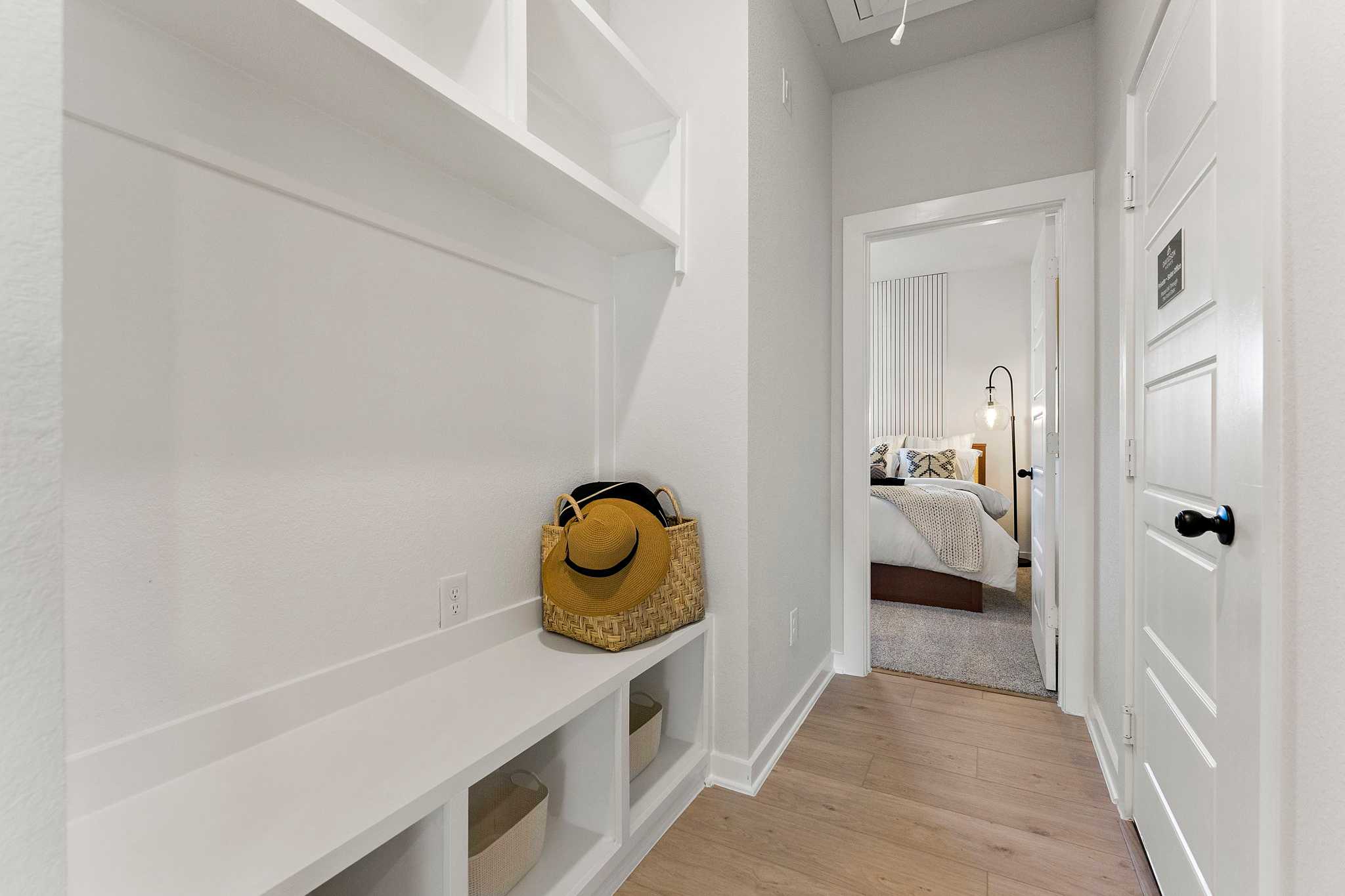 Spacious mudroom with white built-in bench and shelves at Sundance Cove in Crosby Texas, yellow bag and hat, open to bedroom