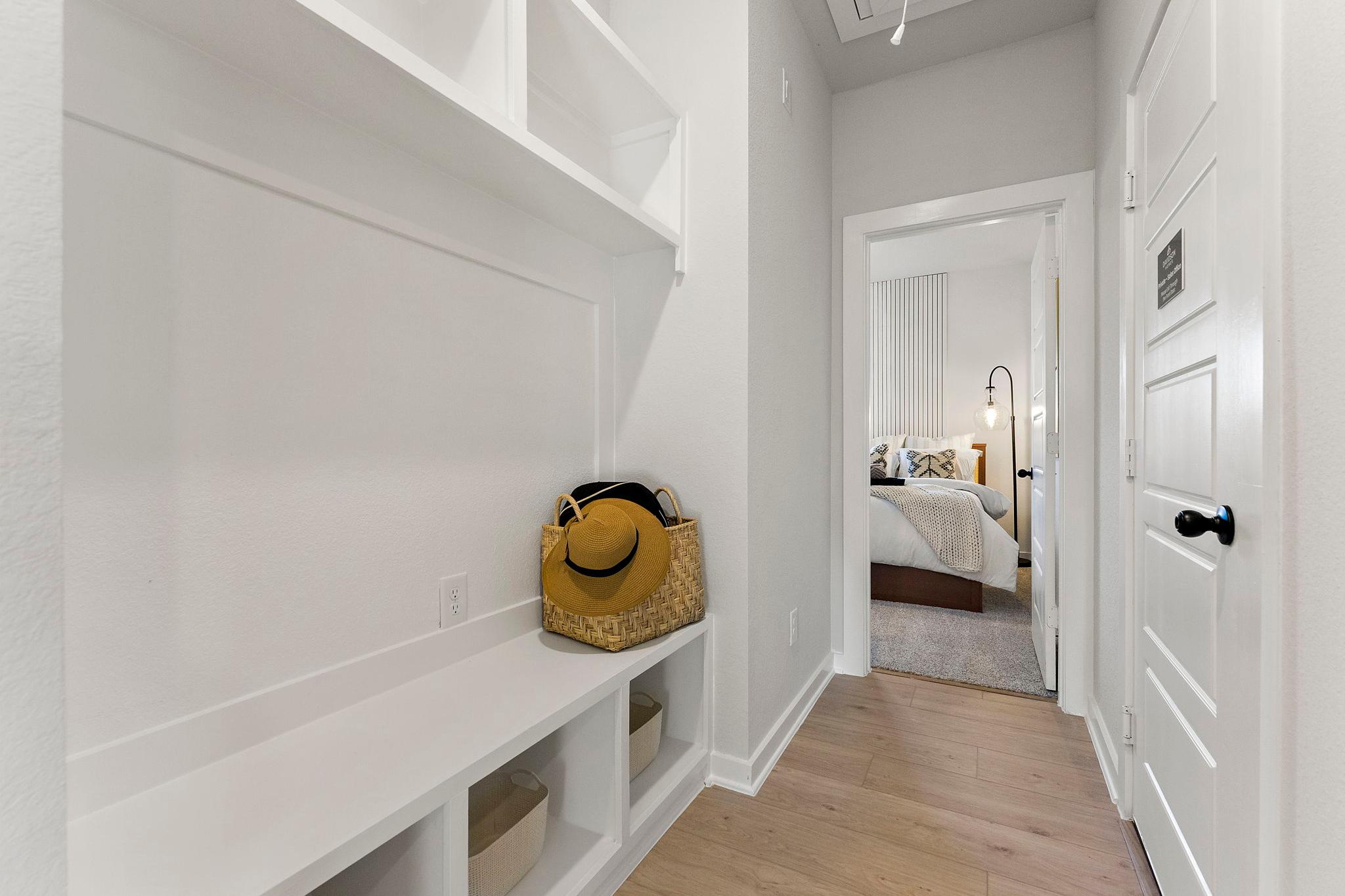 Spacious mudroom with white built-in bench and shelves at Sundance Cove in Crosby Texas, yellow bag and hat, open to bedroom