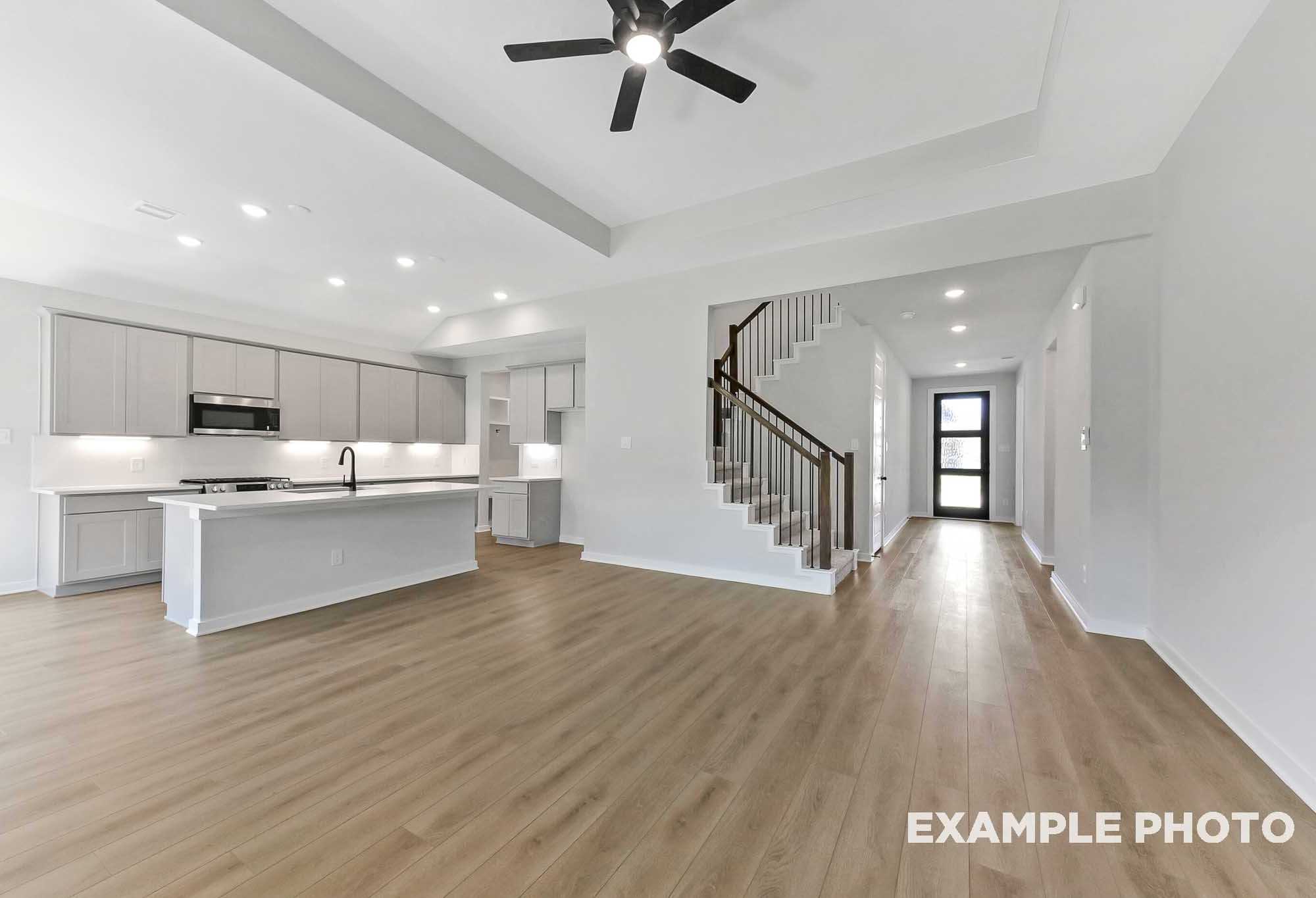 Open-concept kitchen and living area in The Sequoia home design with white cabinets, large island, hardwood floors, and curved staircase
