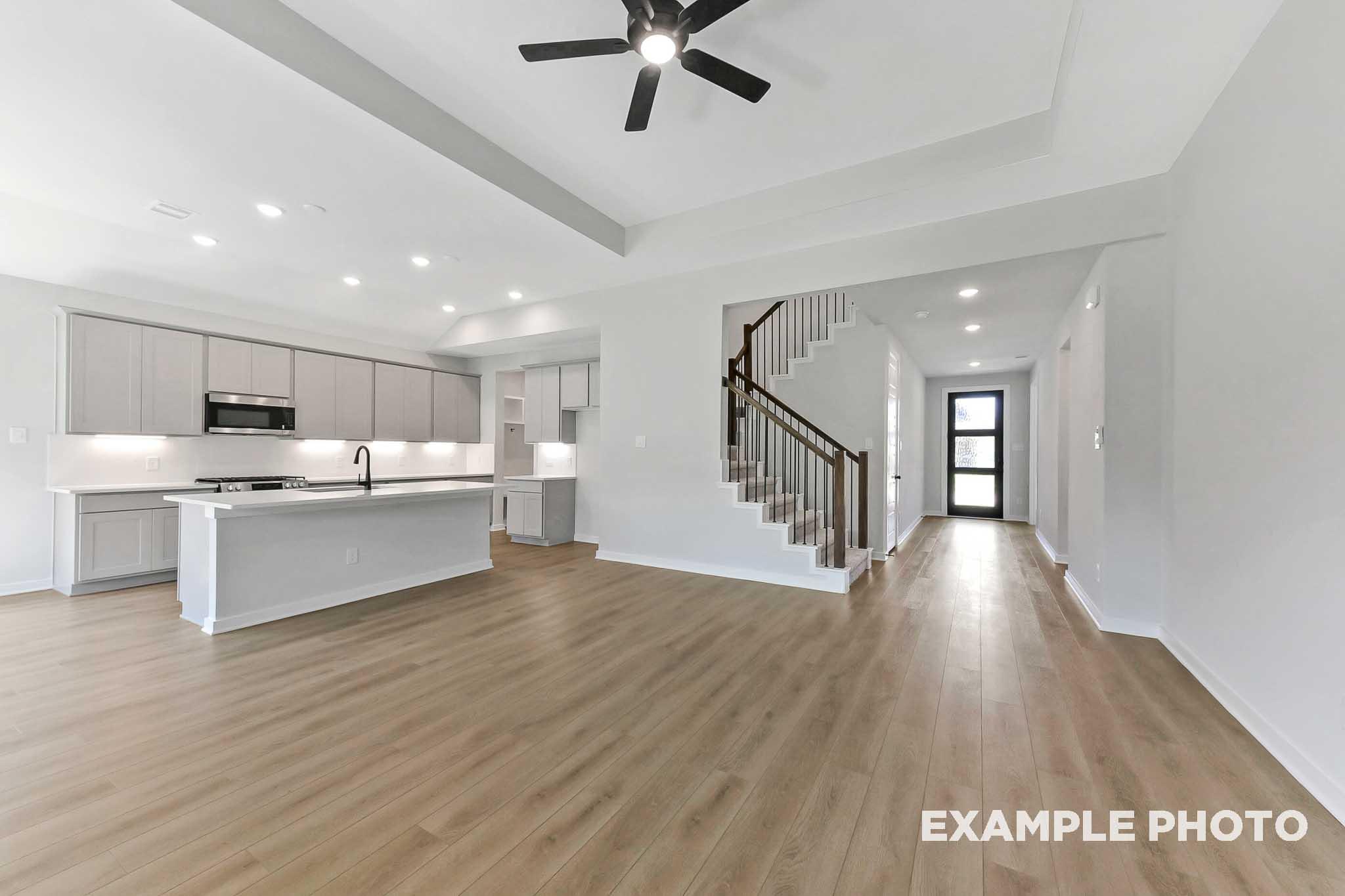 Open-concept kitchen and living area in The Sequoia home design with white cabinets, large island, hardwood floors, and curved staircase