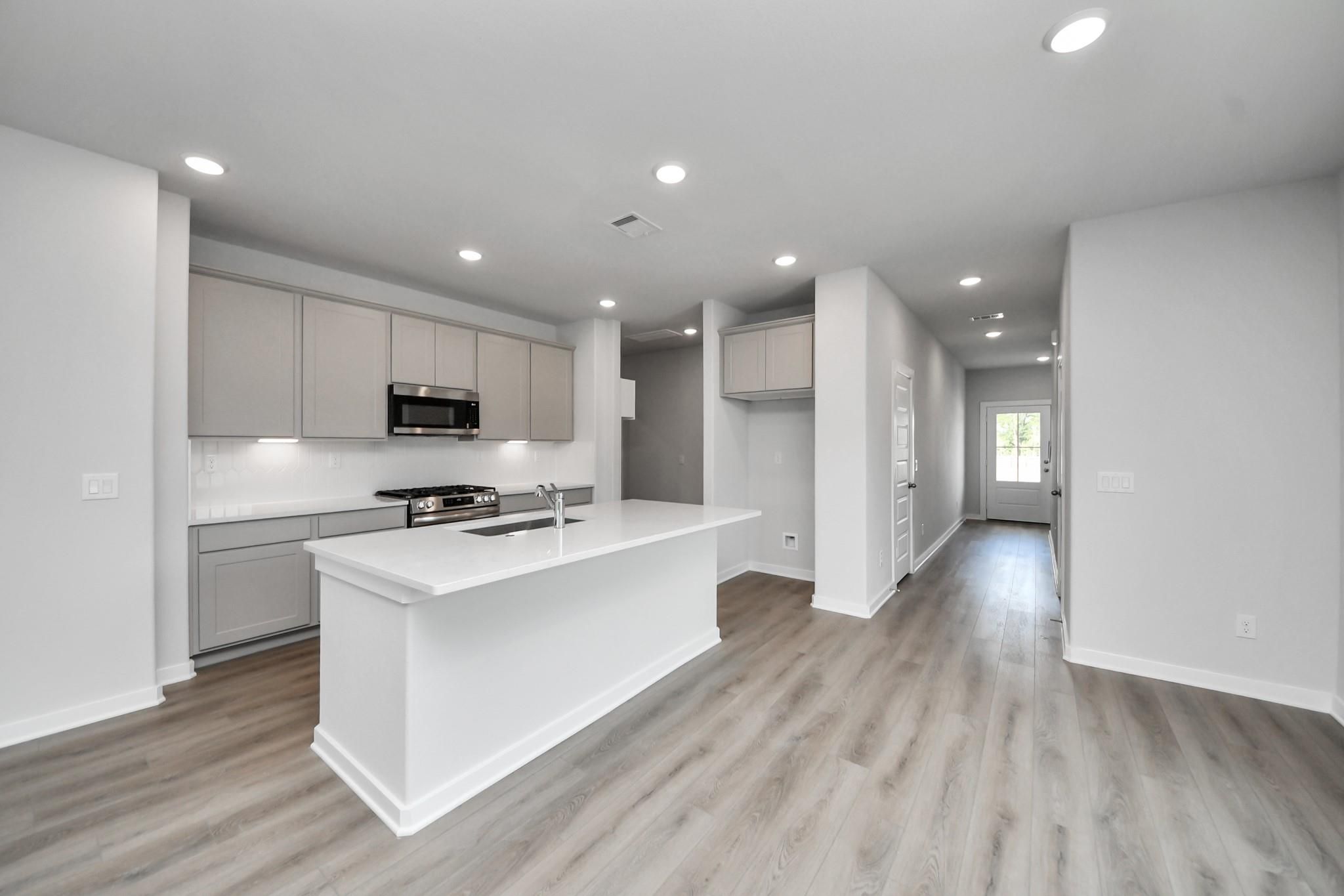 Modern kitchen with white island, gray cabinets, and wood-look flooring in Davidson Homes The Blanco E plan, Magnolia, Texas