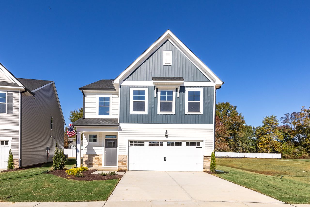 Modern two-story home exterior in Gregory Village, Lillington NC with covered porch, white garage doors, and autumn trees