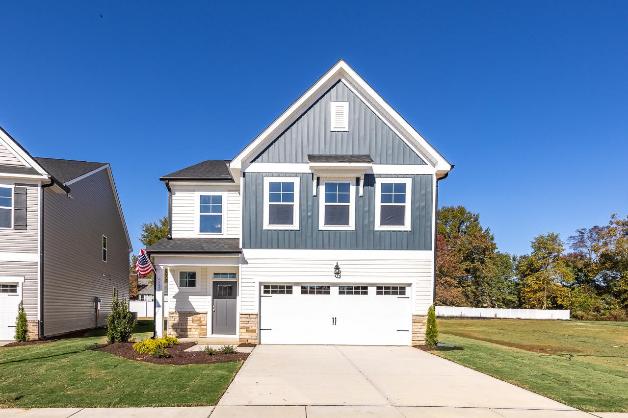 Modern two-story home exterior in Gregory Village, Lillington NC with covered porch, white garage doors, and autumn trees
