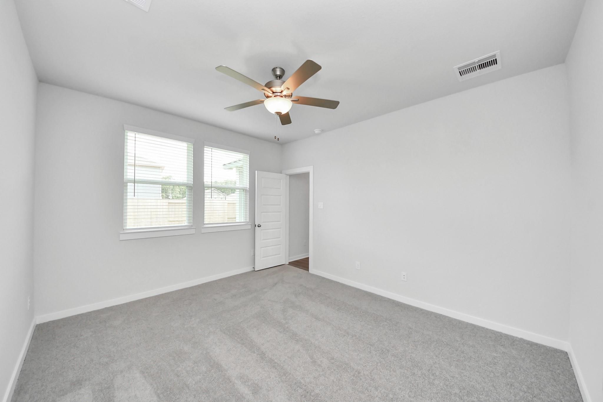 Spacious bedroom with grey carpet and ceiling fan in The Brazos F floor plan at Liberty Estates, Cleveland, Texas.