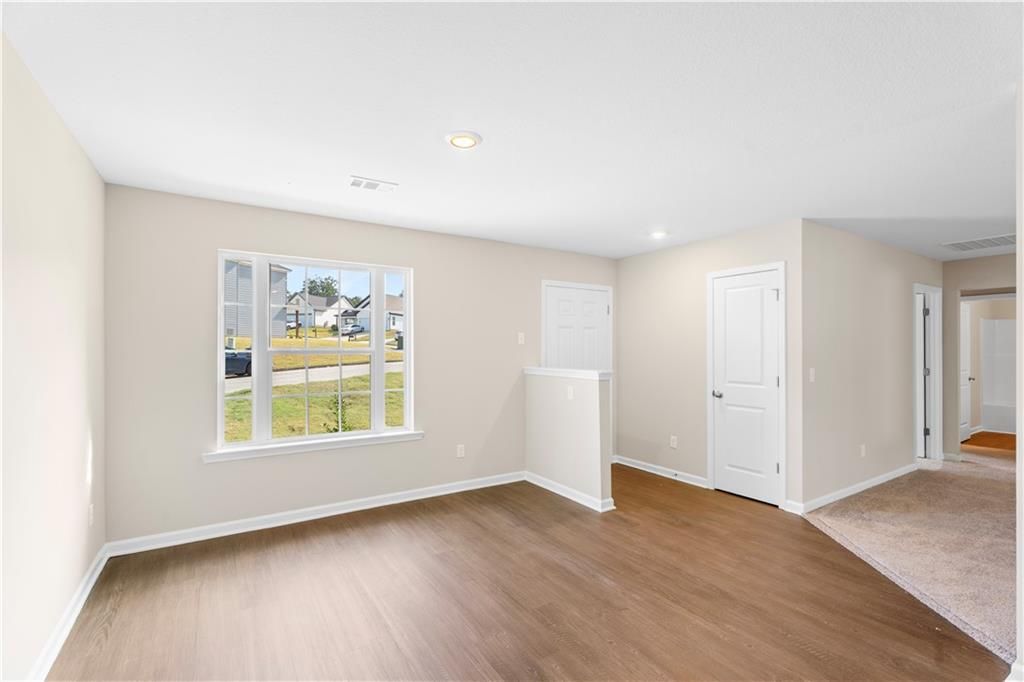Bright secondary bedroom with large window overlooking green lawn, beige walls, hardwood floors in Davidson Homes The Washington, Phenix City, Alabama