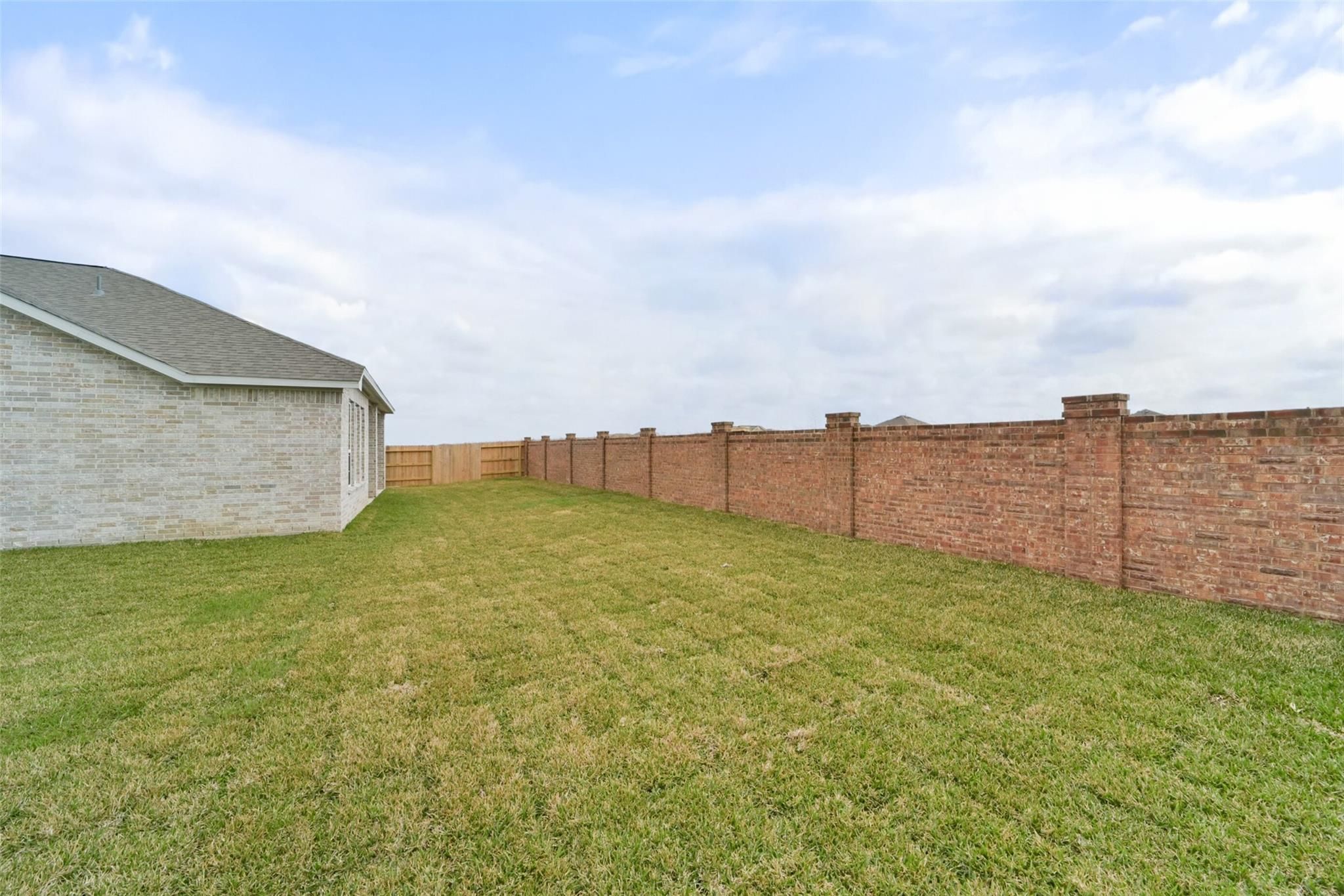 Spacious green backyard with lush lawn, tall brick privacy fence with pillars, and beige house in Davidson Homes The Zion A, Lago Mar, Texas