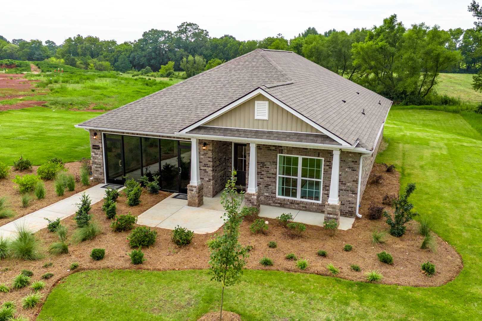 Single-story brick ranch home exterior at The Meadows in Athens Alabama with covered porch, side garage, and lush landscaped yard