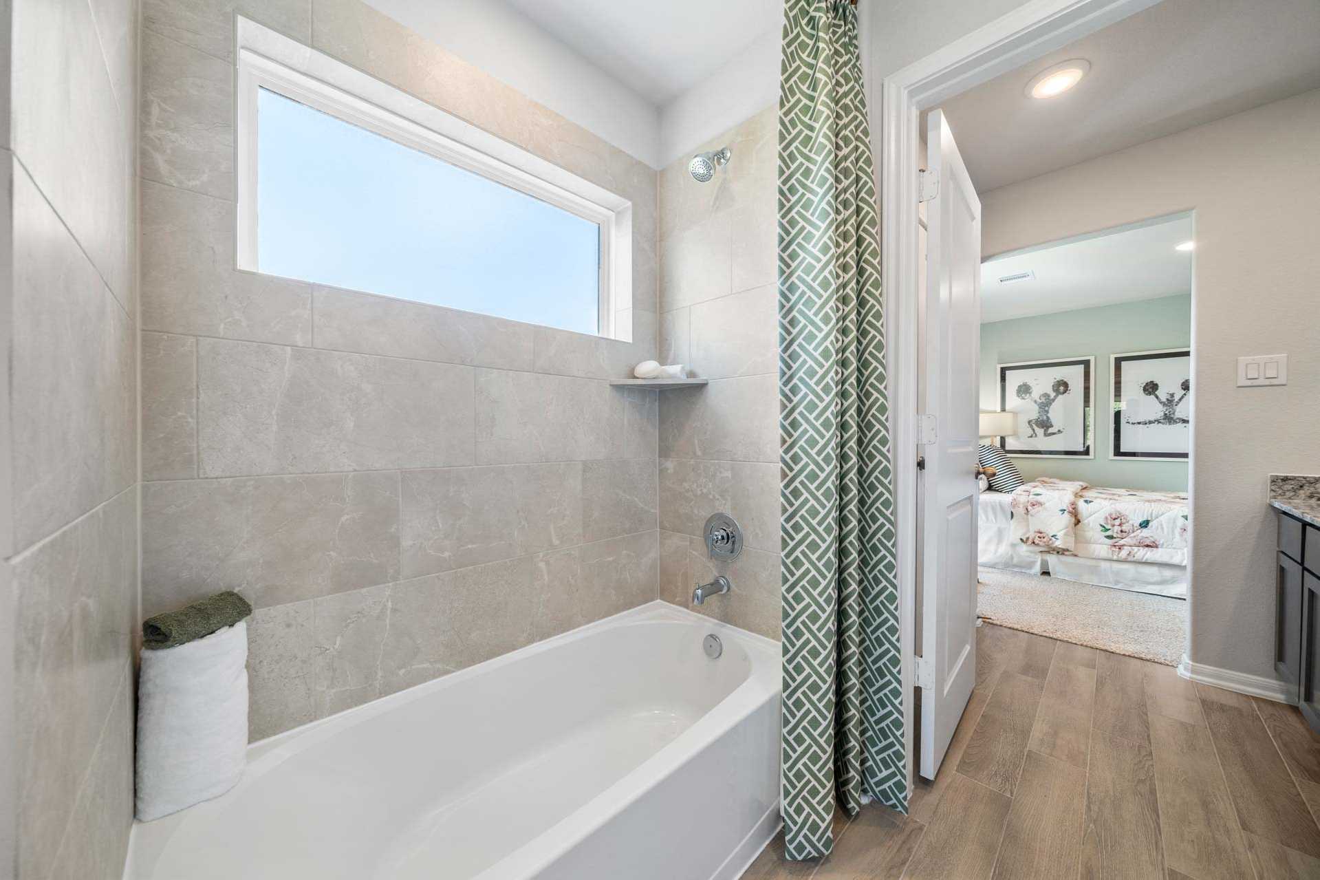 Spacious bathroom at Windmill Estates in Magnolia Texas with soaking tub, green shower curtain, and bedroom view