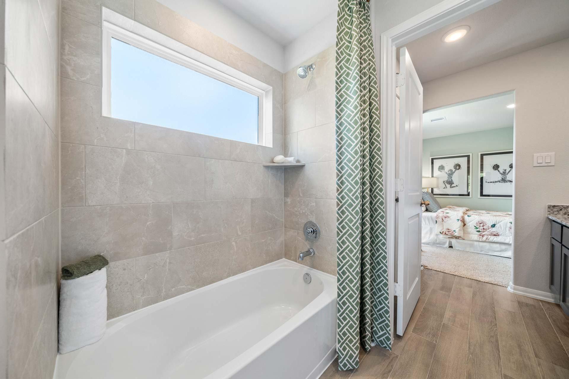 Spacious bathroom at Windmill Estates in Magnolia Texas with soaking tub, green shower curtain, and bedroom view