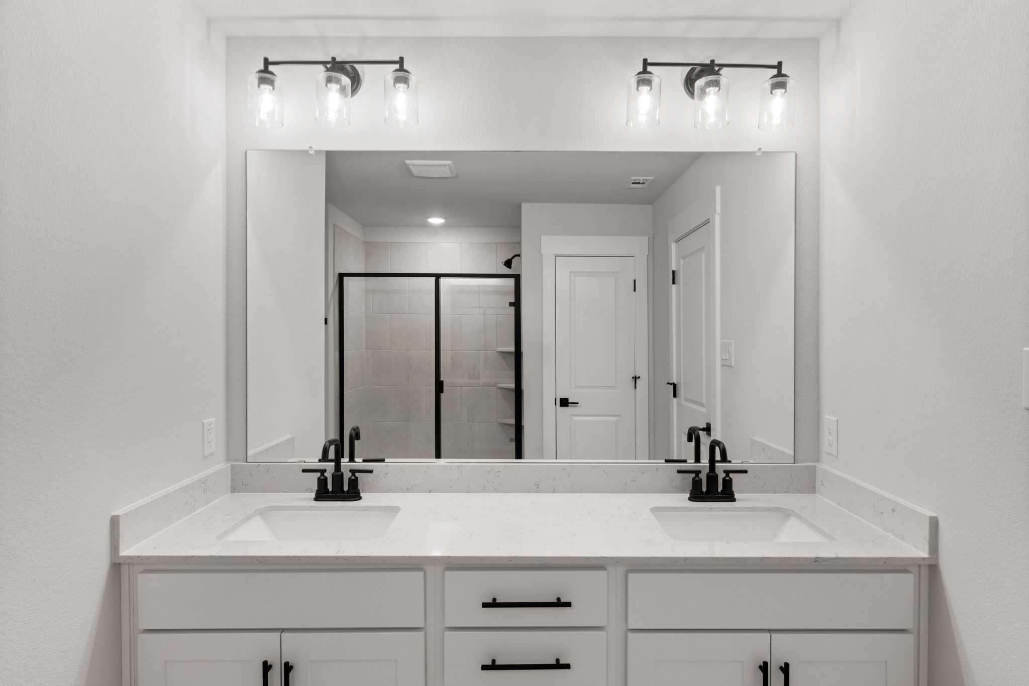 Modern master bathroom with double white vanity, black faucets, large mirror, and glass shower in Davidson Homes The Durham E, Wylie, Texas