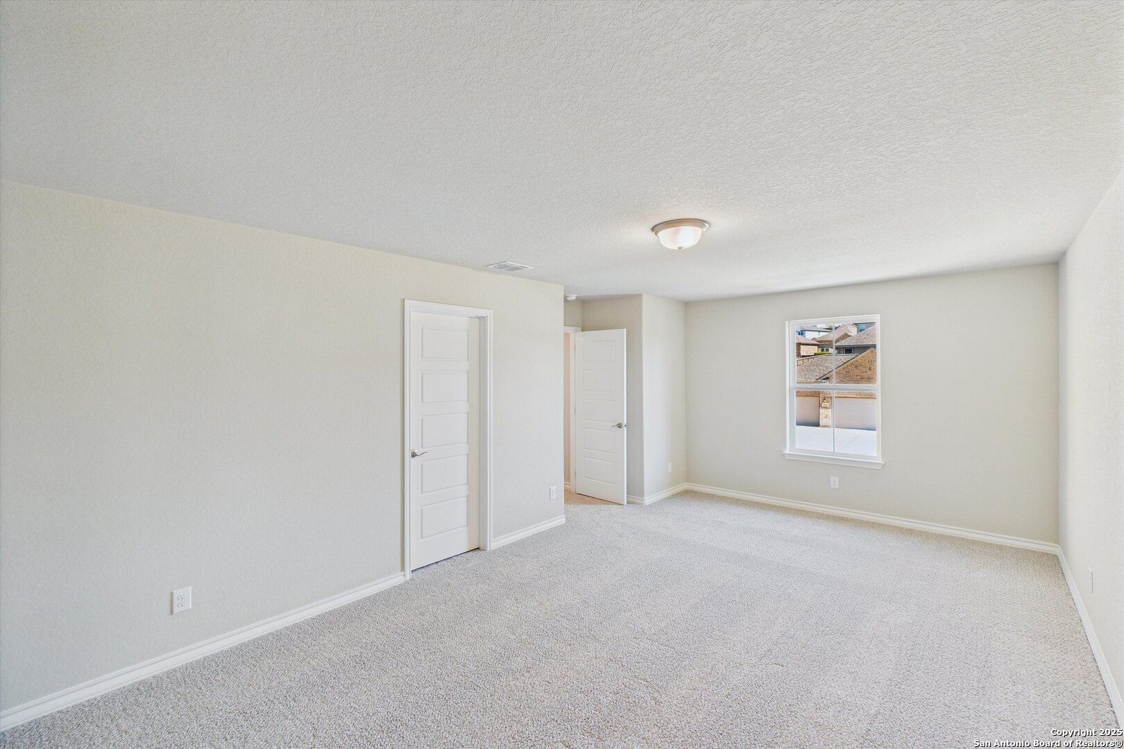 Spacious empty bedroom with beige walls, carpet floor, window, and bath door in Davidson Homes The Jennings H, Ladera, San Antonio